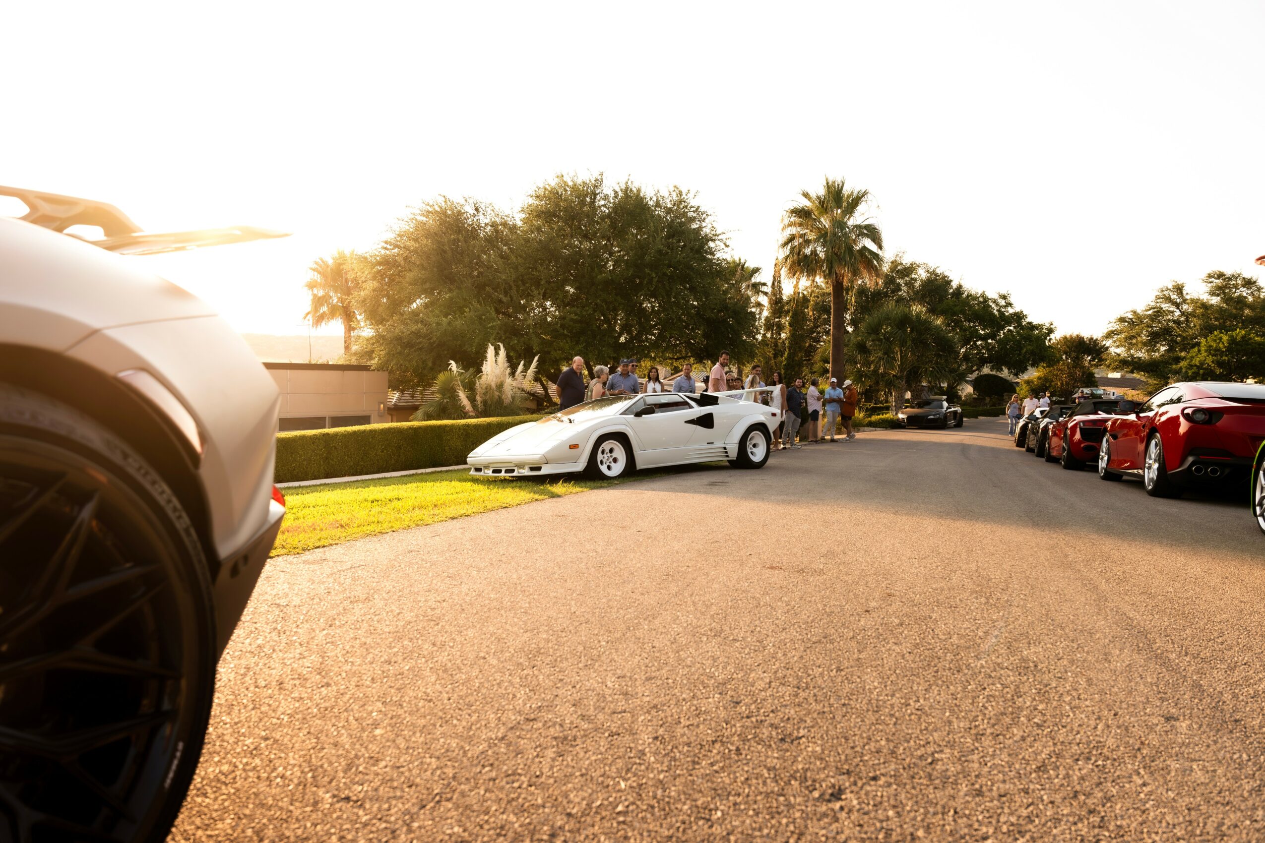 White sports car parked on a street with trees and other cars in the background.