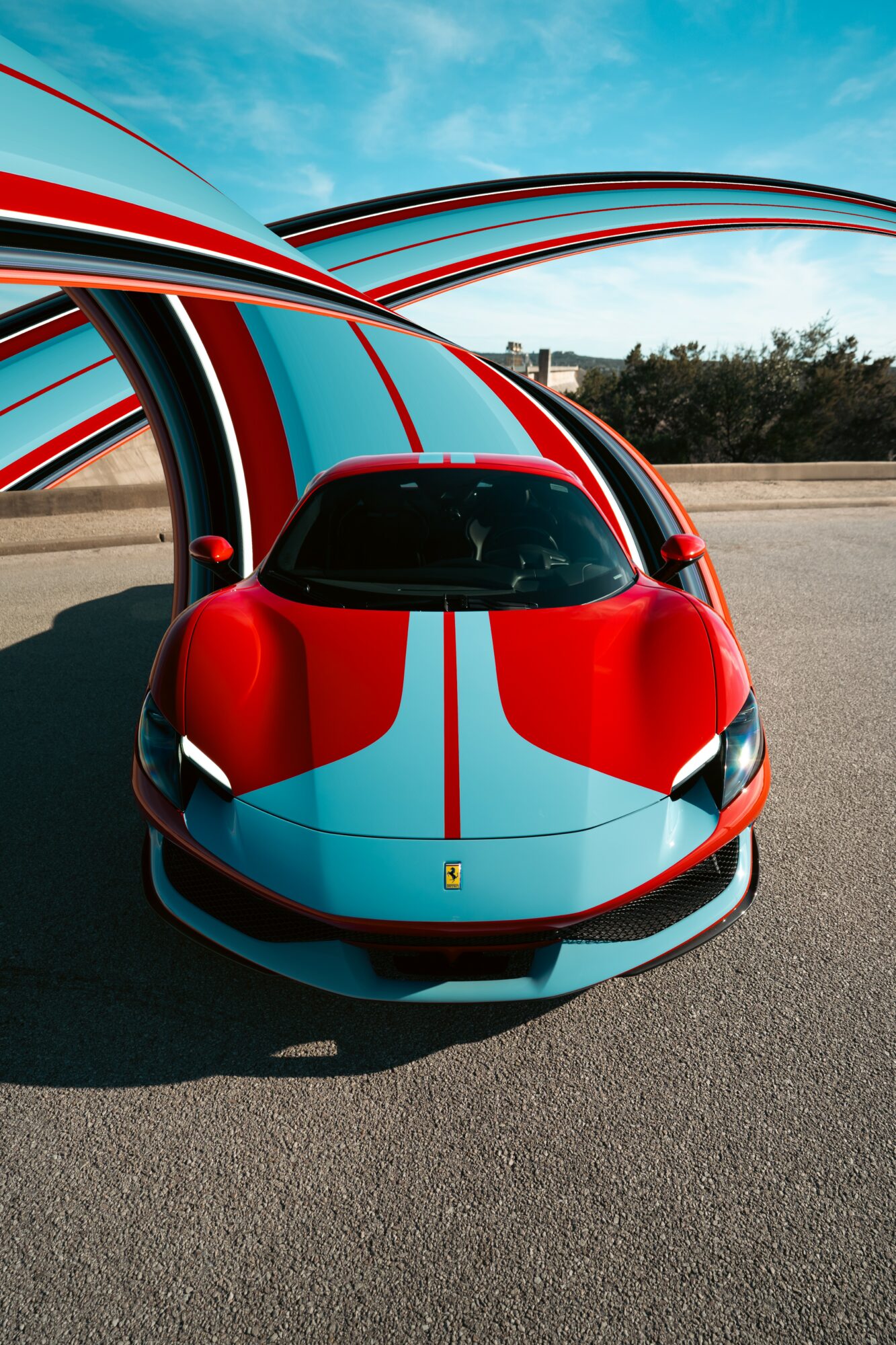 Red and blue sports car parked on asphalt with curved structures and a blue sky background.