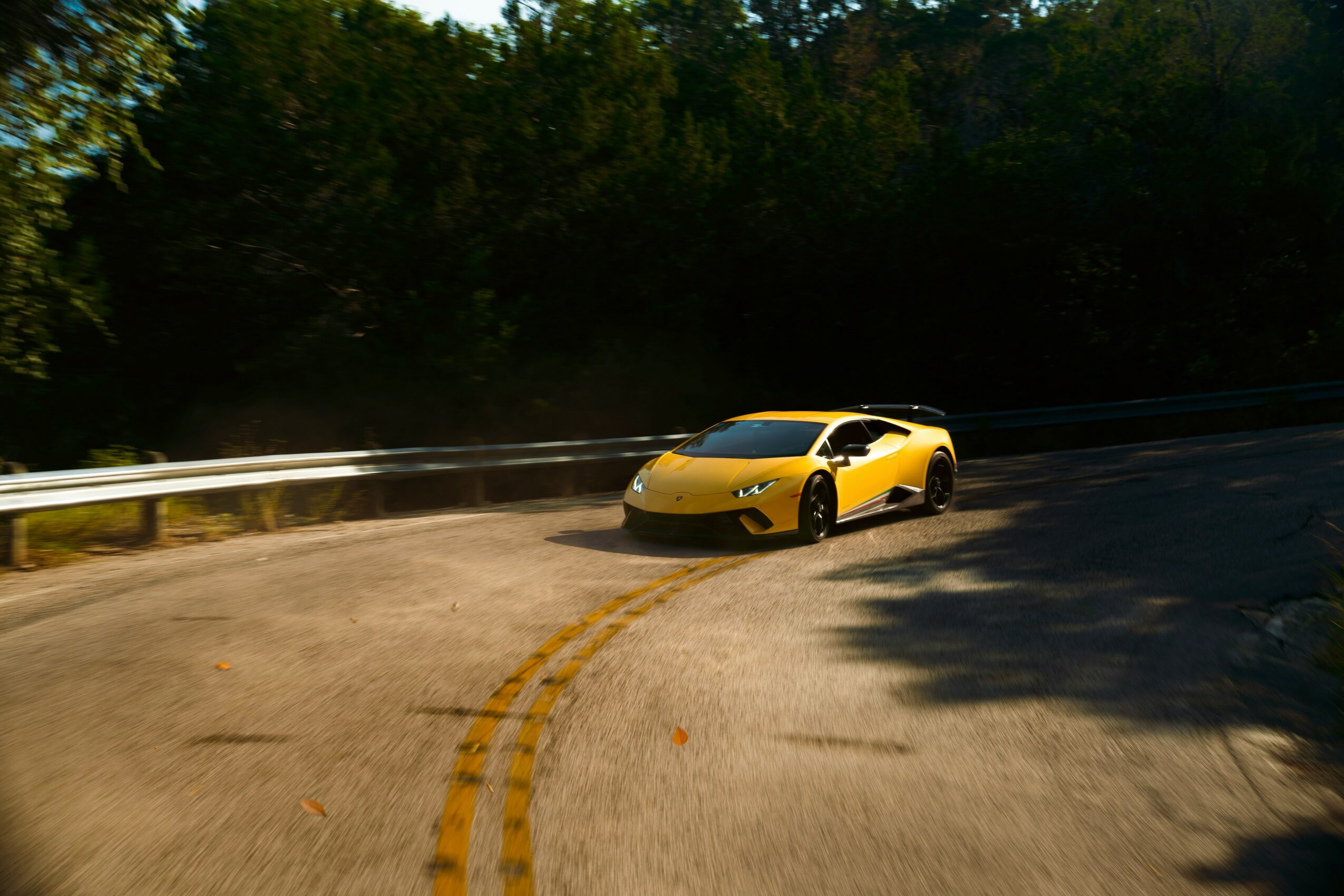 Yellow sports car parked on a curved road with trees and shadows in the background.