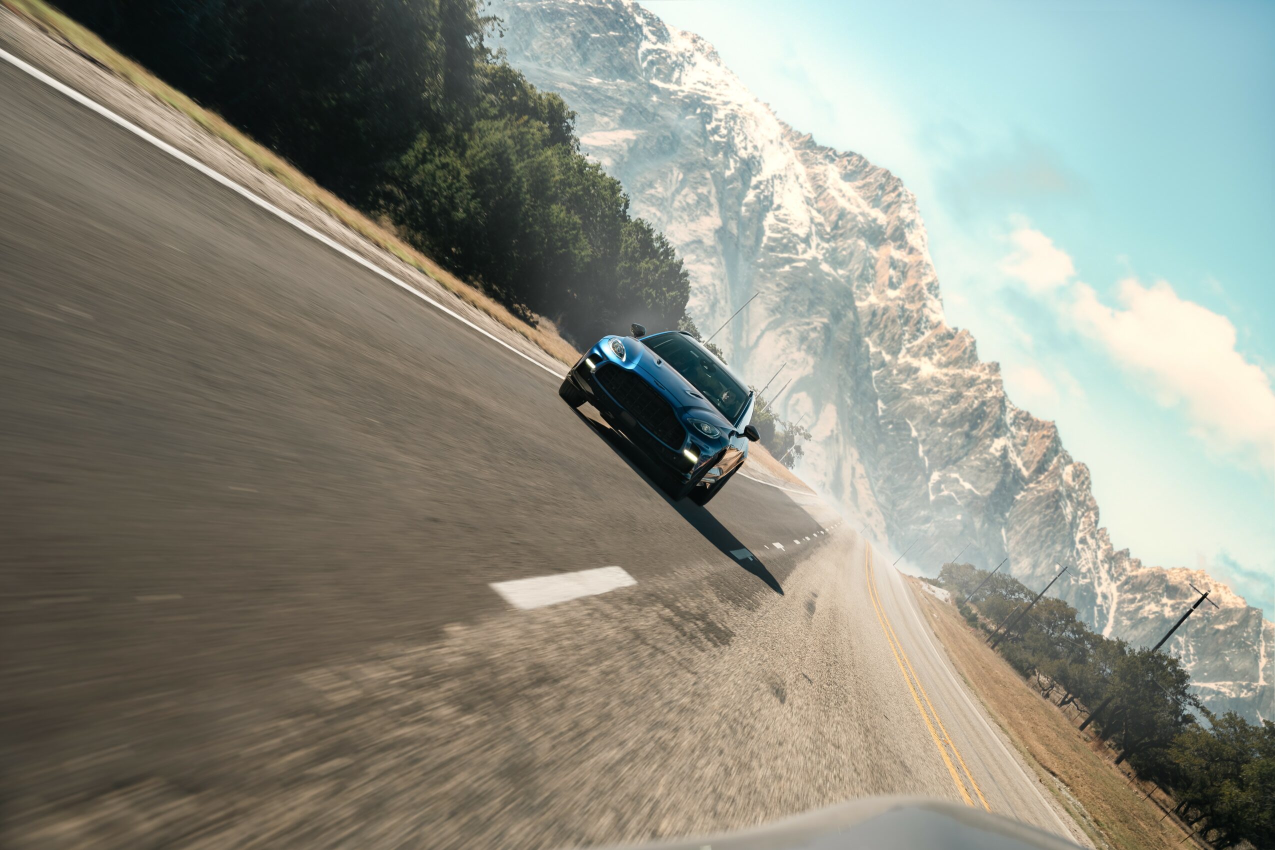 Black car driving on a mountain road with snow-covered peaks in the background, tilted to the right.