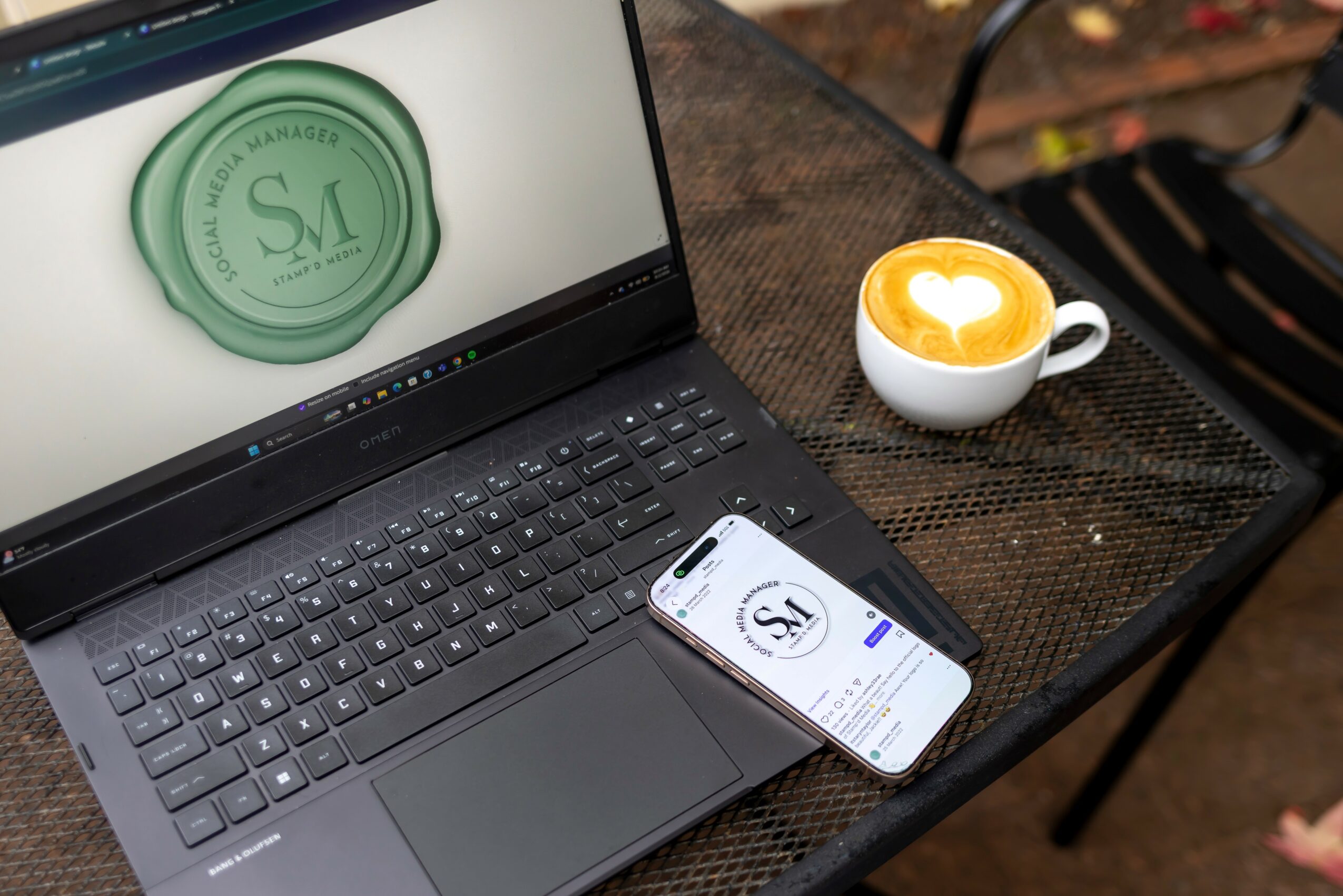 Laptop, smartphone, and coffee cup on a table, with a wax seal design on the laptop screen.