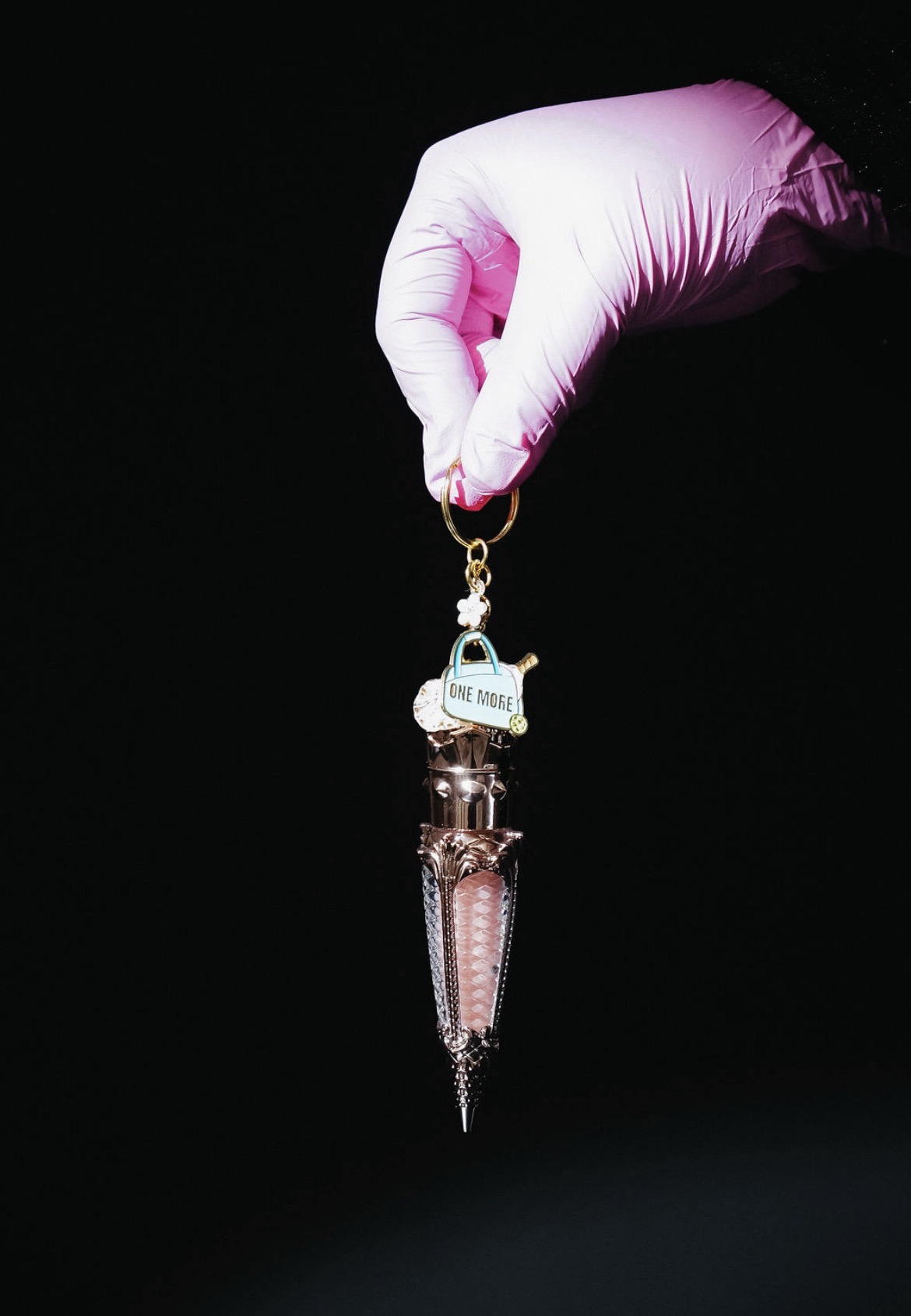 Hand in pink glove holding a pendant with a small umbrella and a tag, against a black background.