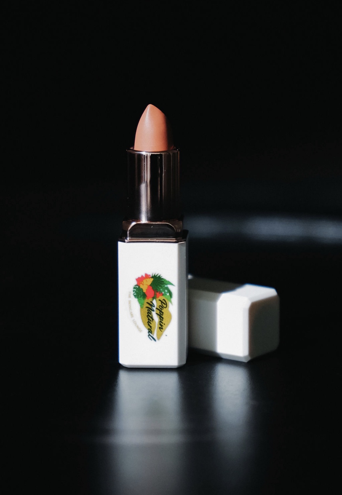 Lipstick with a white case featuring a colorful pineapple design, cap removed, on a dark background.