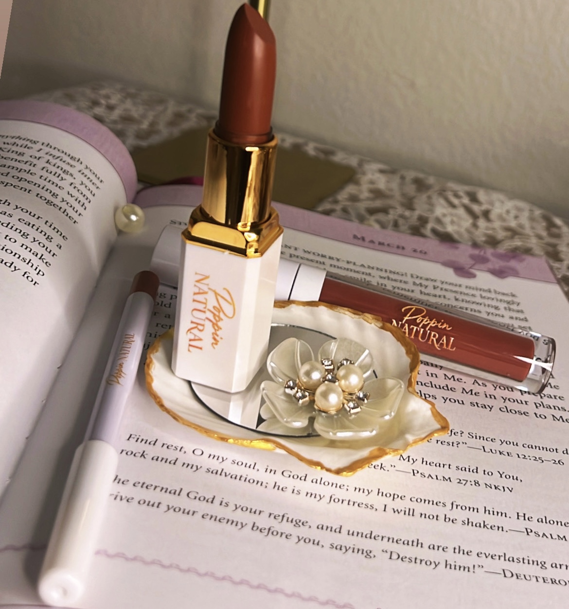 Lipstick, nail polish, pen, and decorative pearl accessories on an open book surface.