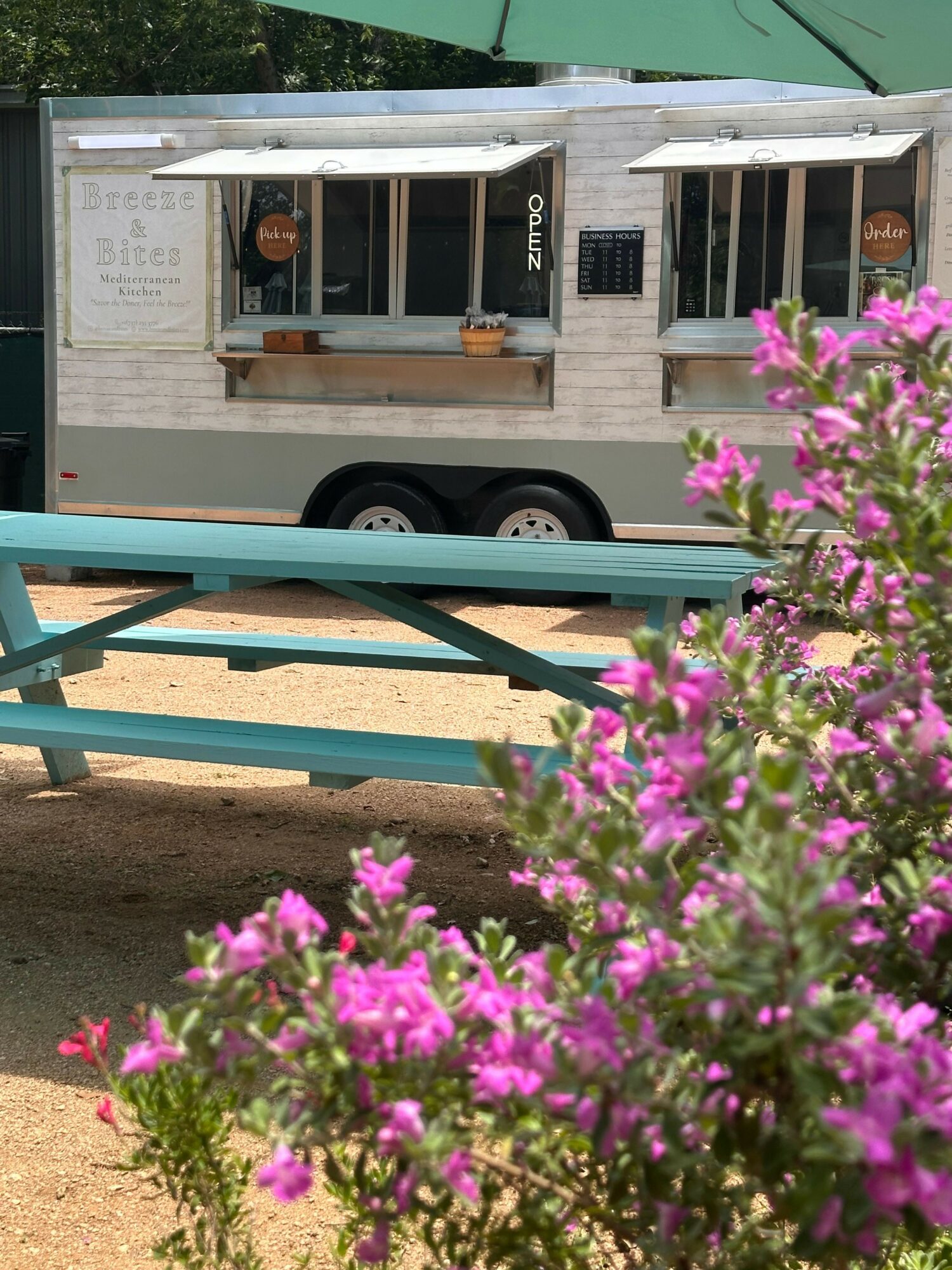 Pink flowers in foreground with a food truck in the background, showing a menu and a window.