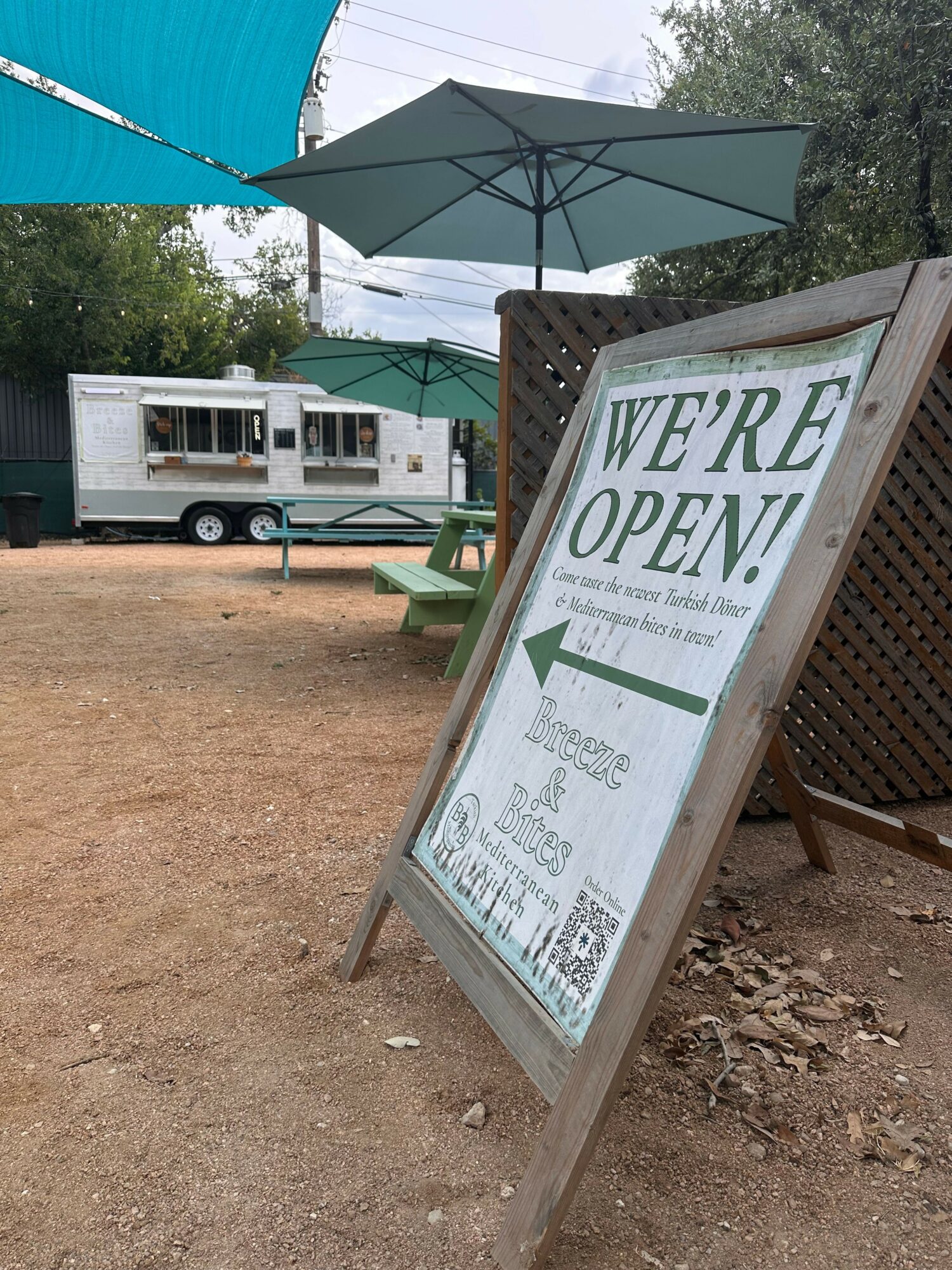 A signboard with an arrow pointing to the left, indicating the business is open, placed outdoors on dirt ground.