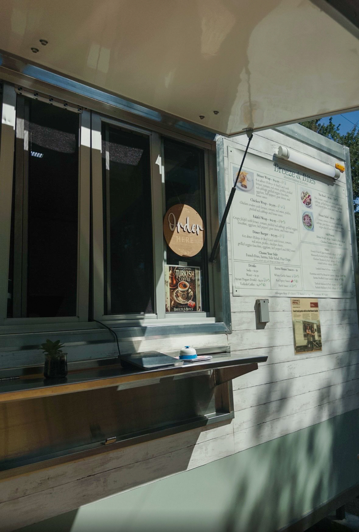 Window with menu and sign outside a building, sunlight casting shadows, part of a counter or shelf below.