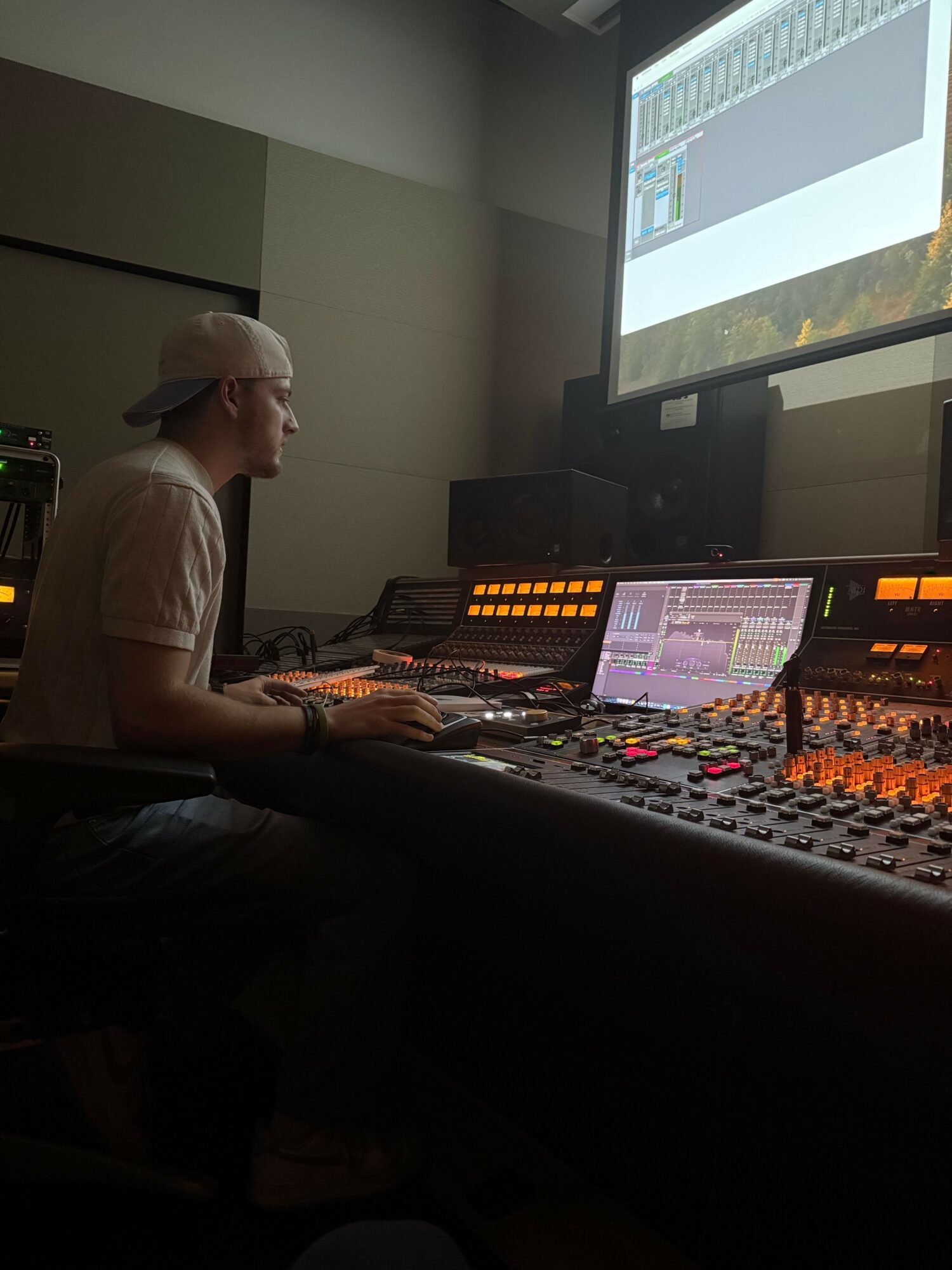 Person wearing a white hat working at a music production console in a studio.