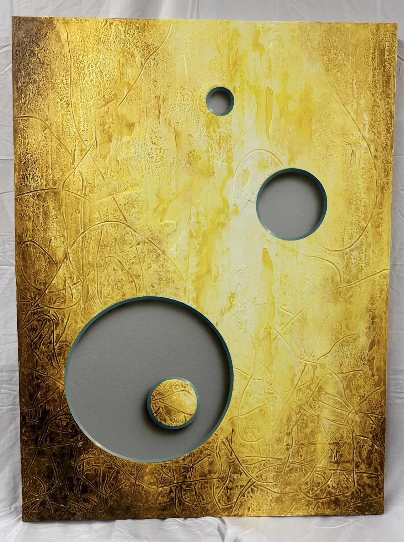 Rectangular gold-colored textured surface with three circular cutouts of different sizes, one with a yellow object inside.