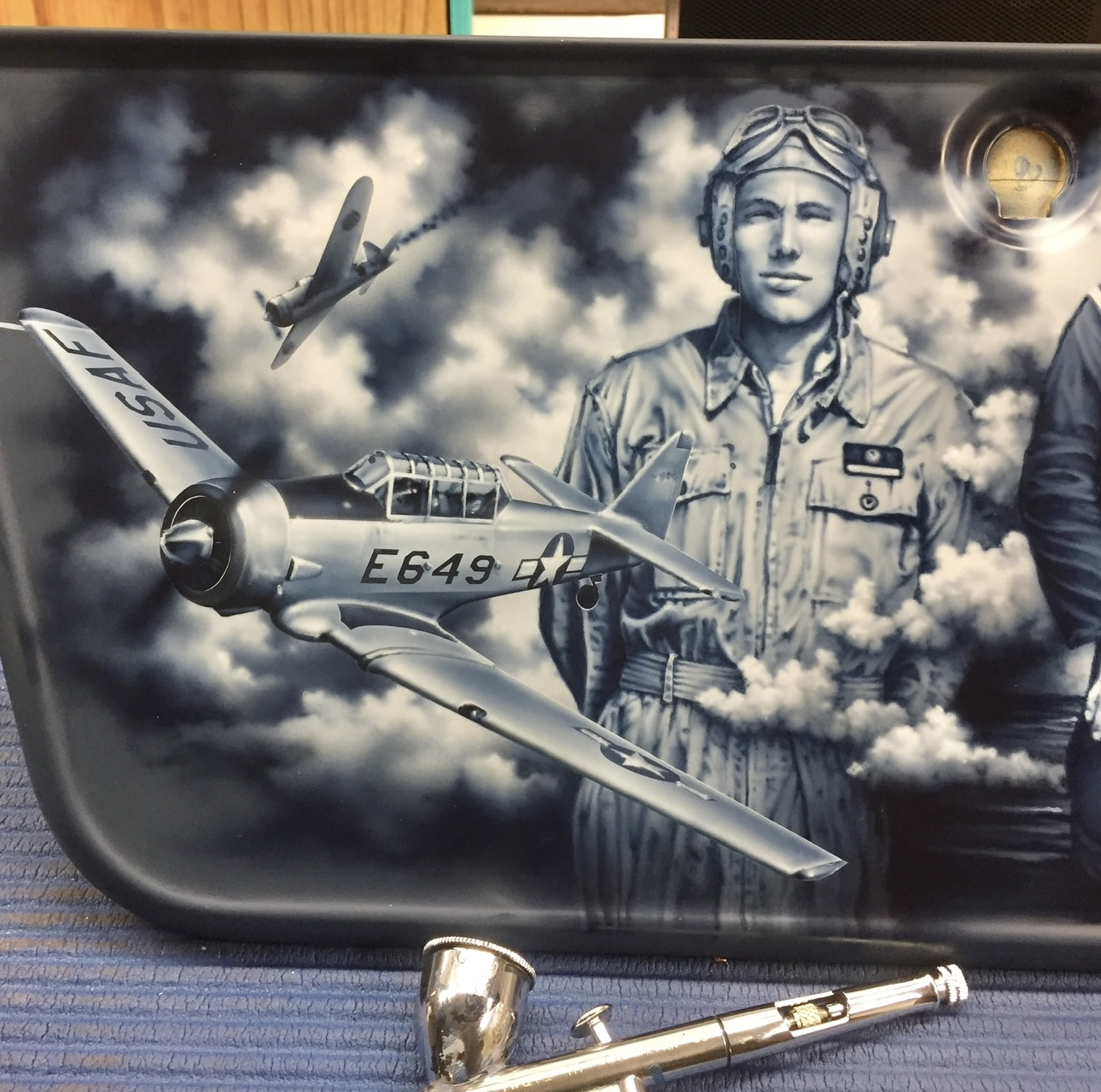 Black and white mural of a female pilot in uniform, a fighter jet, and an airplane flying through clouds.