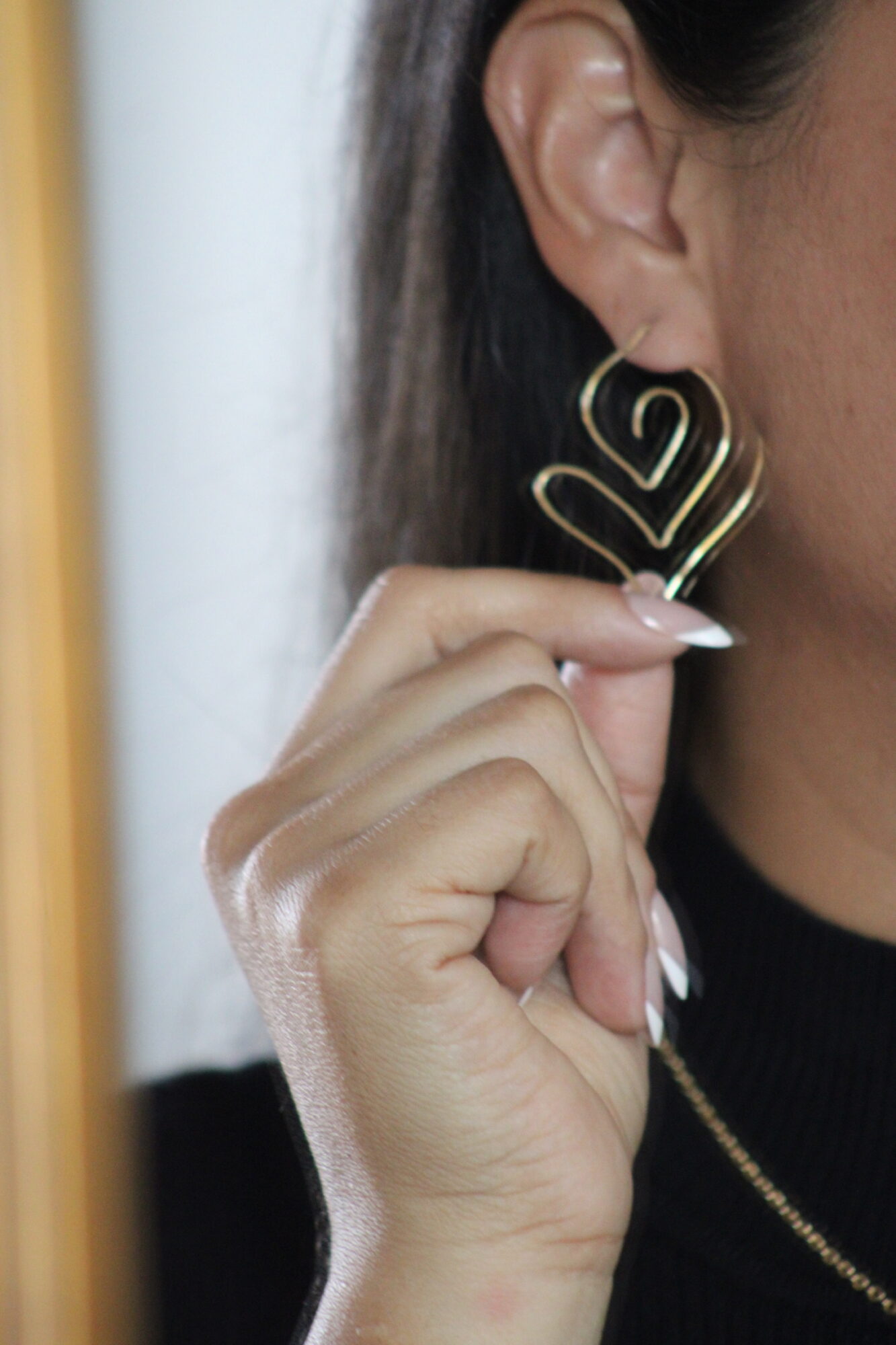 Close-up of a person holding a gold earring with a heart-shaped design near their ear.