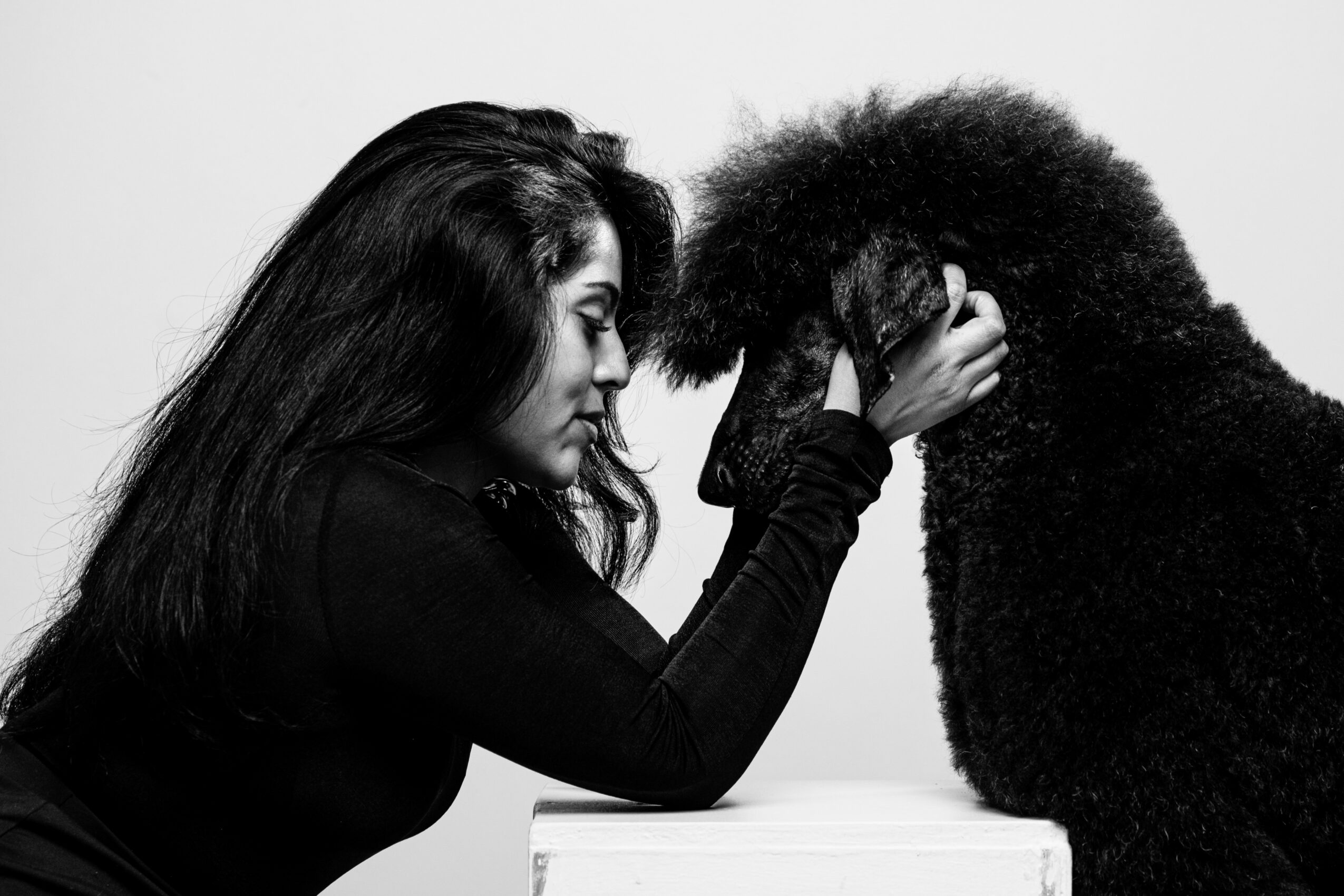 Woman gently holds a person's head, both leaning toward each other, in black and white. Word count: 20.