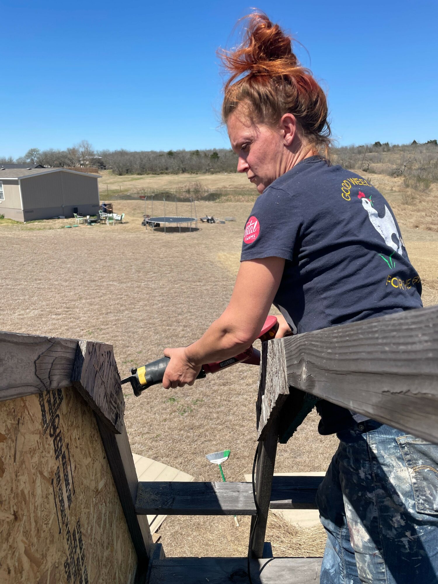 Person working outdoors on a wooden structure, with a clear sky and open landscape in the background.