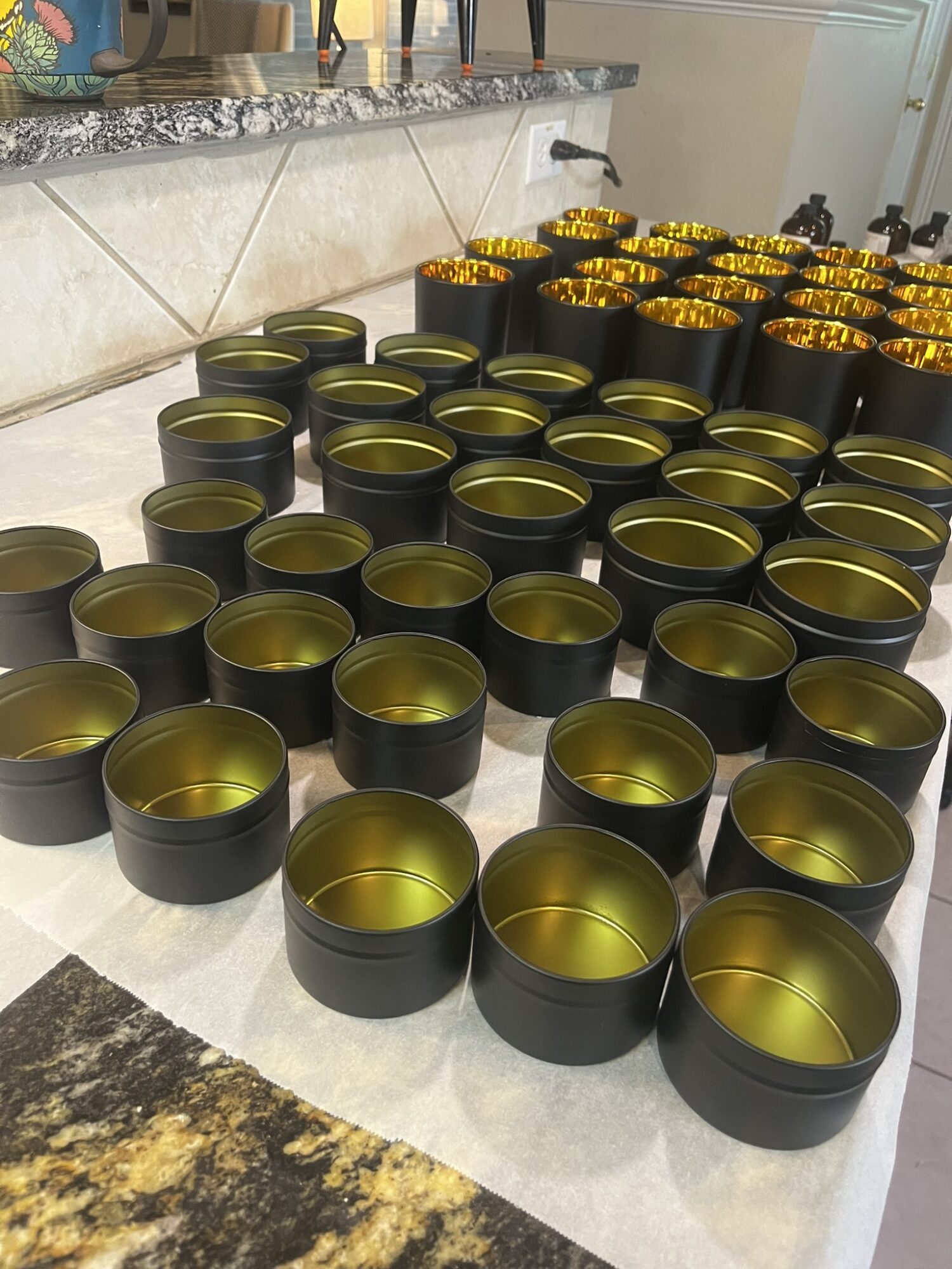 Multiple black containers with gold interiors arranged on a kitchen counter, some filled with yellow liquid.