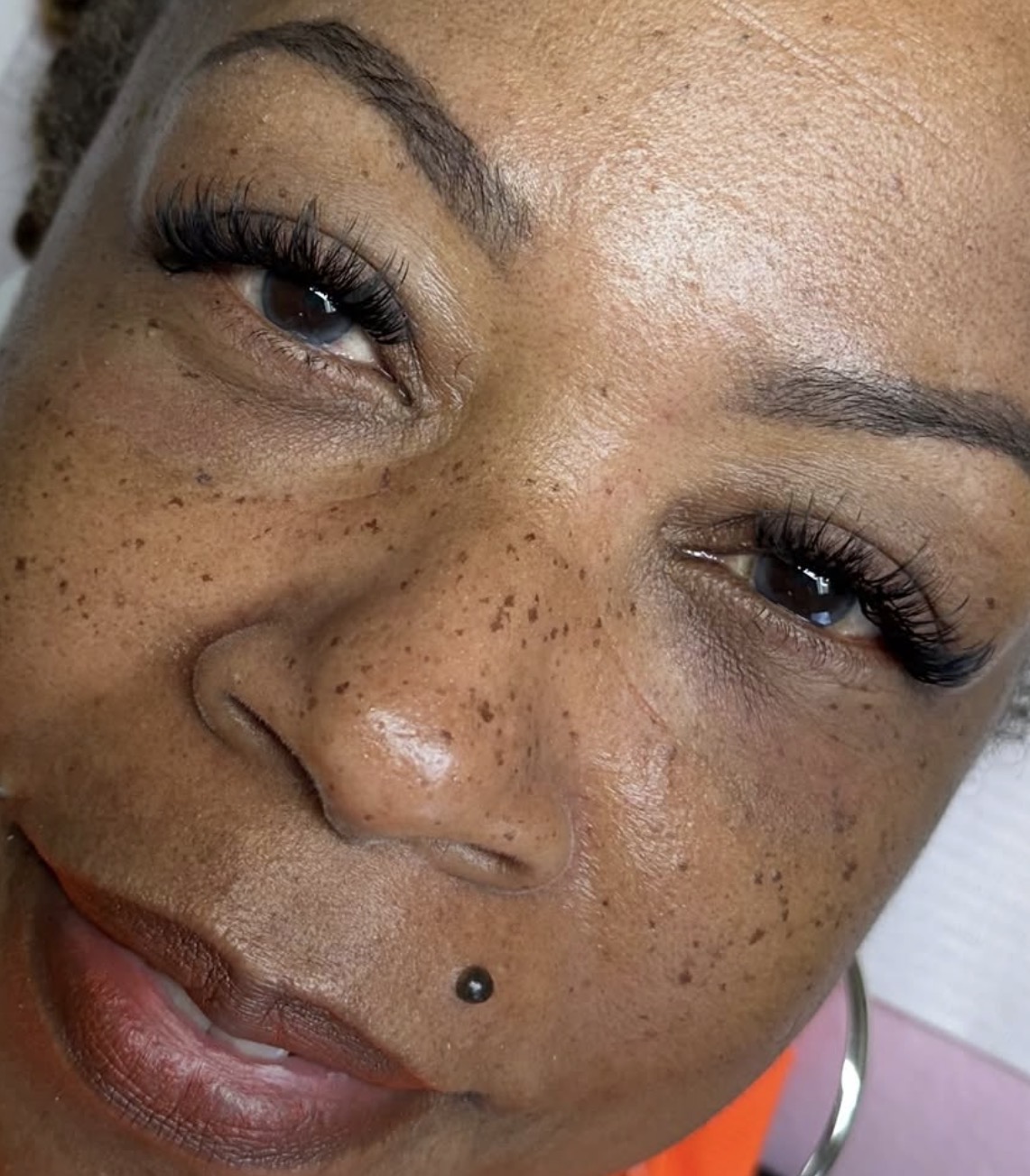 Close-up of a woman's face showing freckles, eye makeup, and a nose piercing.