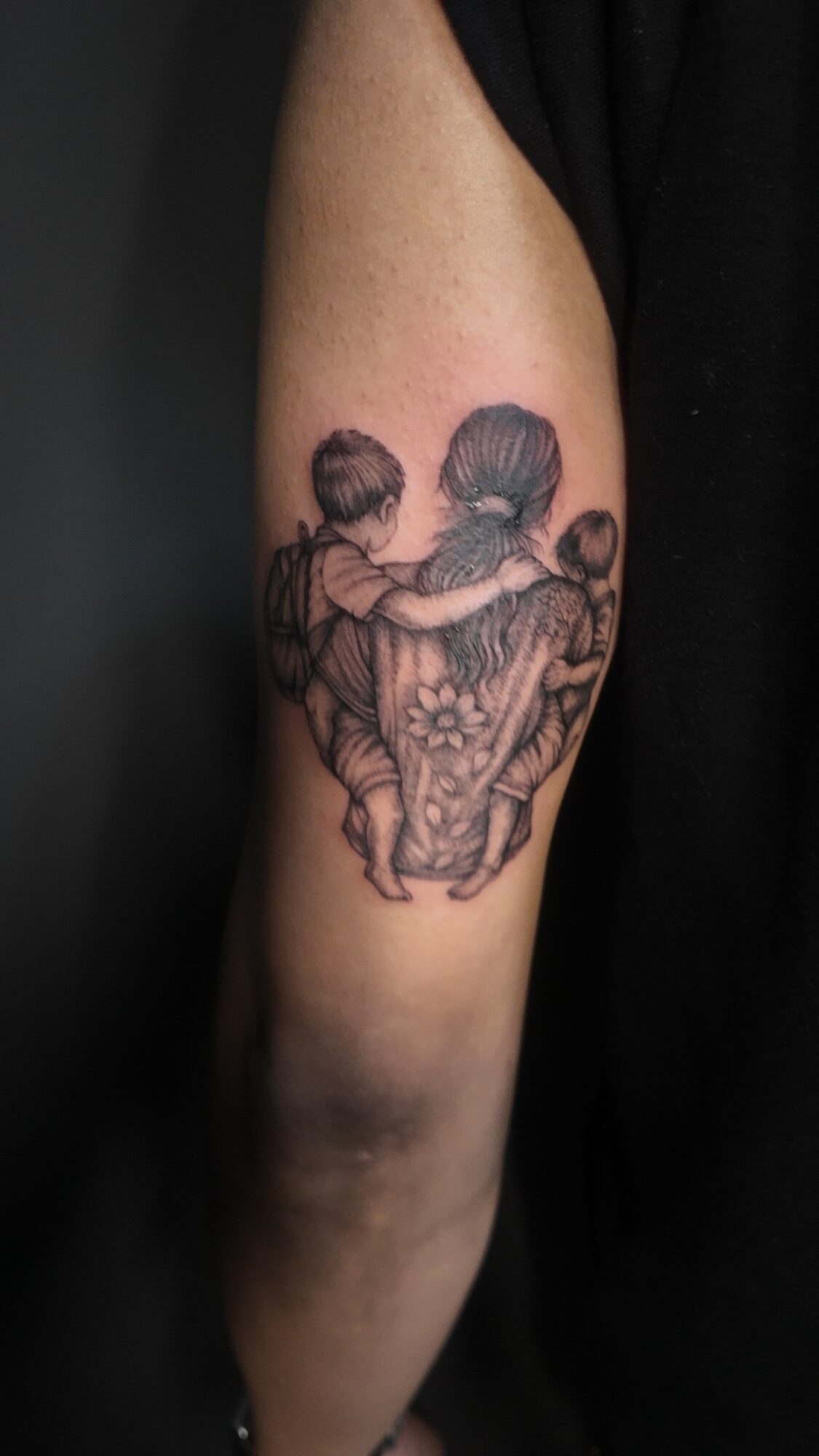 Tattoo of two children hugging, with a butterfly and floral design, on person's upper arm.