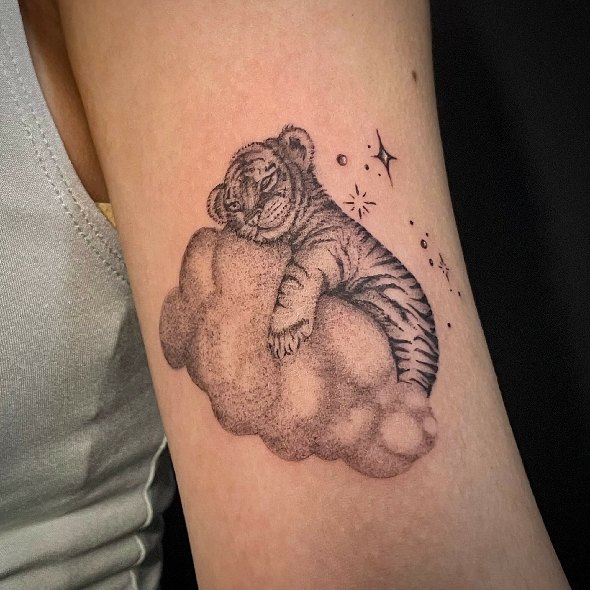 Tiger cub resting on a cloud with stars and sparkles around it, in black ink, detailed linework.