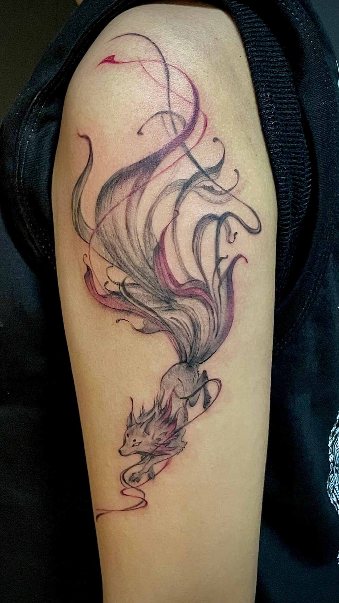 Tattoo of a fox with flowing, wispy tail and smoke-like accents on upper arm.