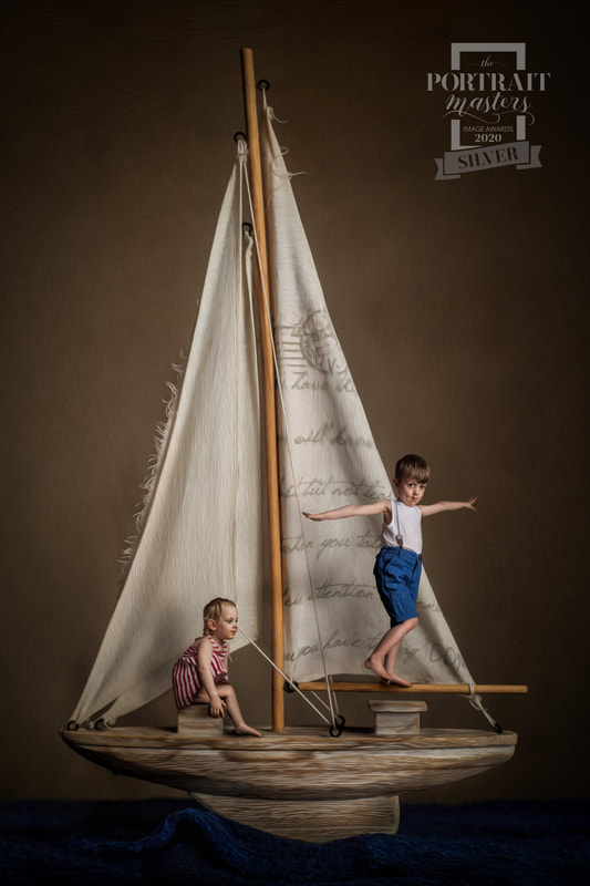 Two children on a boat with a sail, one standing and one sitting, against a dark background.