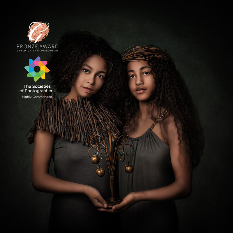 Two women with curly hair hold a decorative plant sculpture against a dark background.