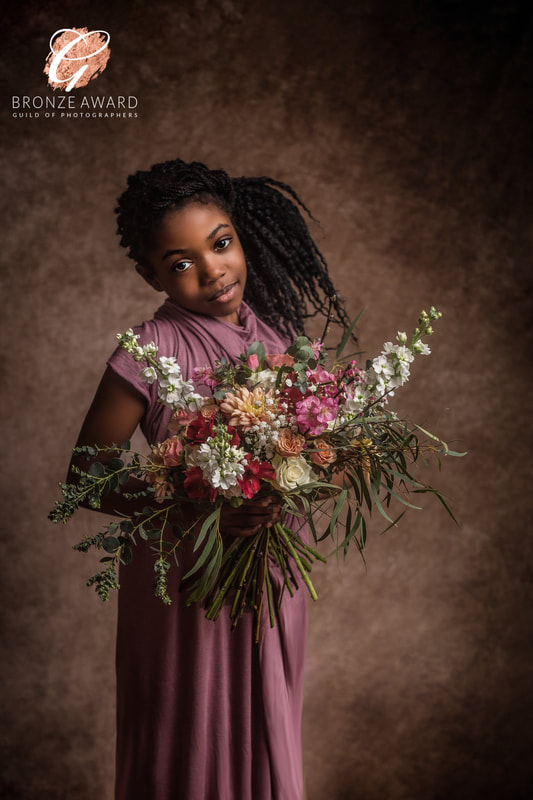 Young girl with braided hair holding a large bouquet of flowers, wearing a pink dress, against a brown background.