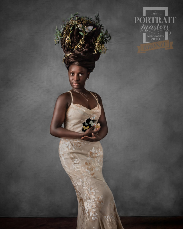 Woman with elaborate floral headpiece in a cream lace dress, standing against a gray background.