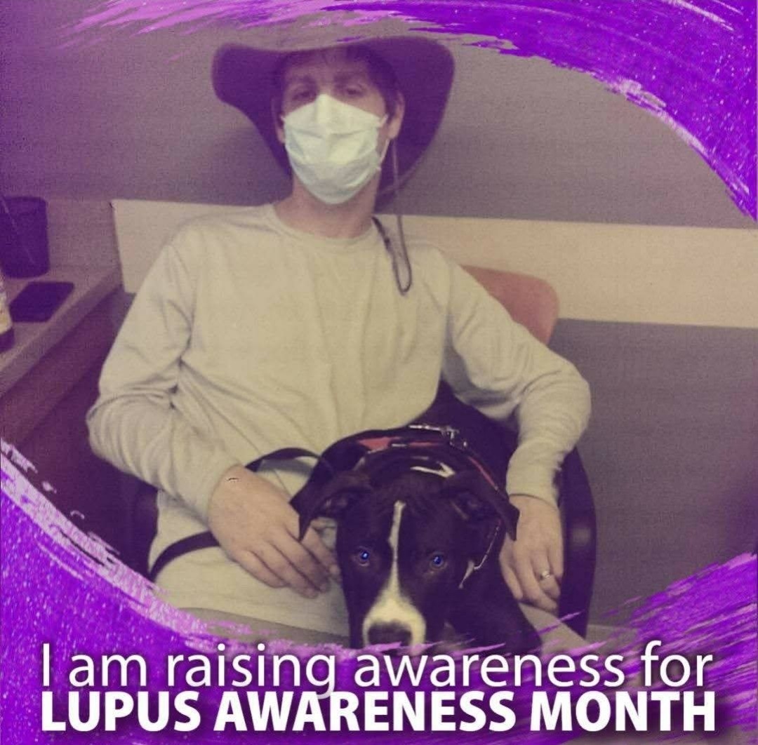 Person wearing a hat and face mask sitting with a dog, promoting Lupus Awareness Month.