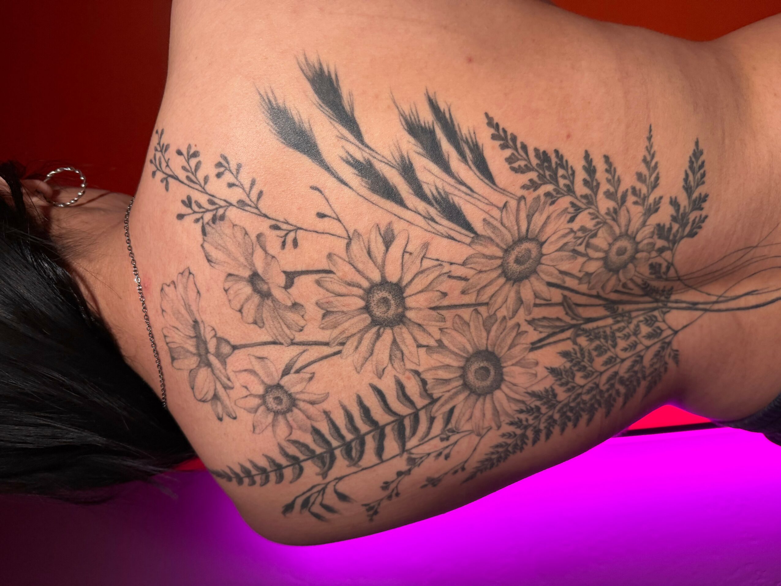 Tattoo of flowers and leaves on person's upper arm, with a pink and purple background.