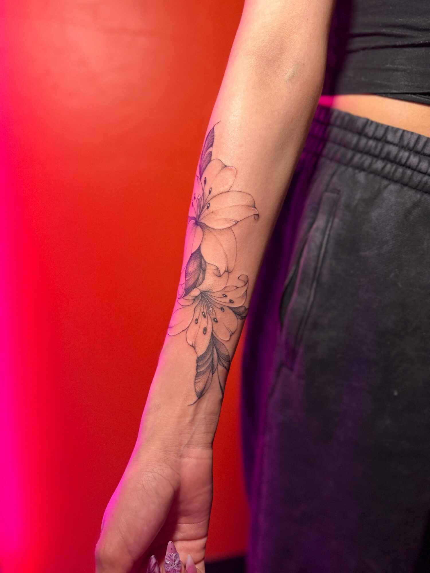 Person's arm with a butterfly and floral tattoo, wearing black pants and a black top, against a red background.