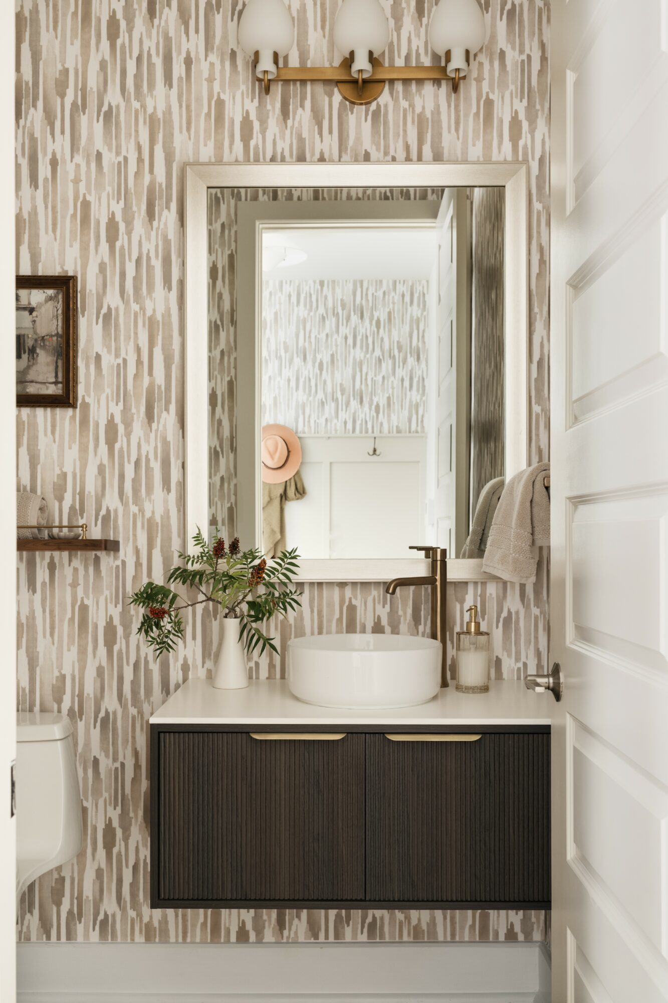 Bathroom vanity with a mirror, sink, and plant, with wallpaper and a wall-mounted light fixture above.