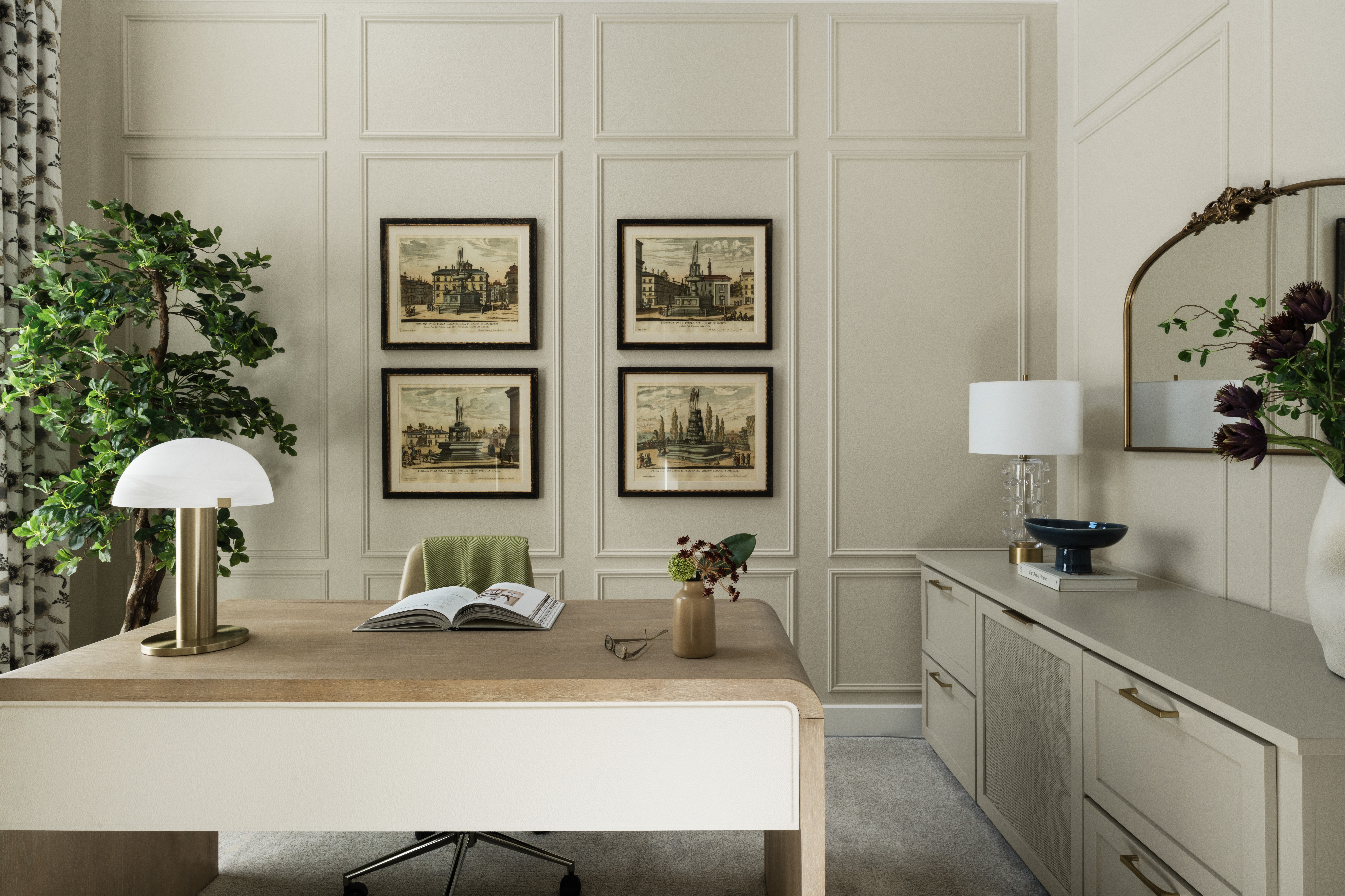 Interior room with wall art, a desk with a lamp, a green chair, and a sideboard with a lamp and decorative items.
