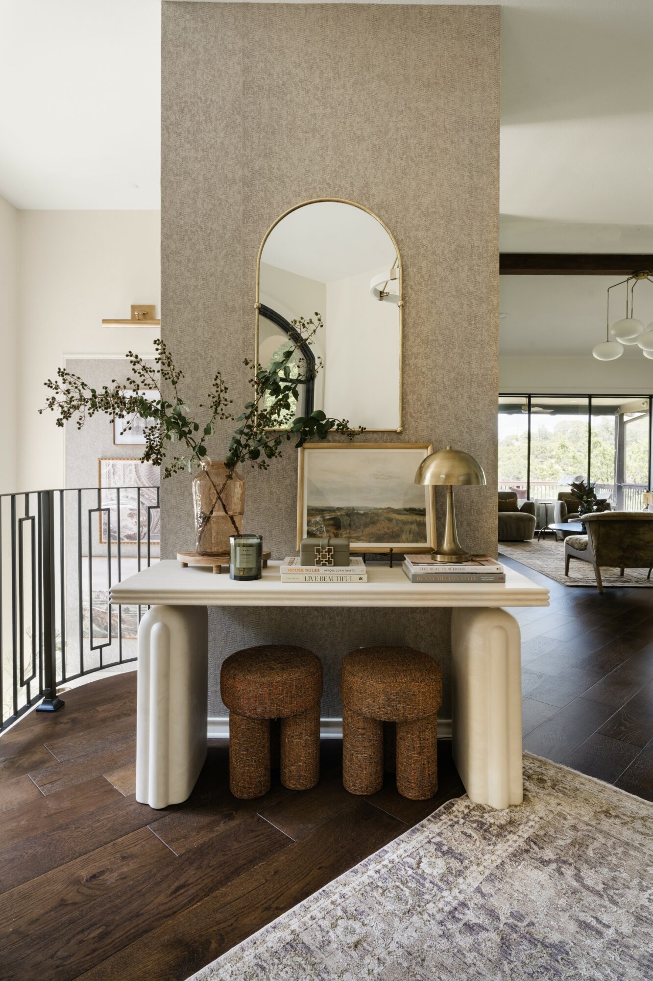 Interior space with a white table, three brown stools, a mirror, and decorative items, with a living area in the background.