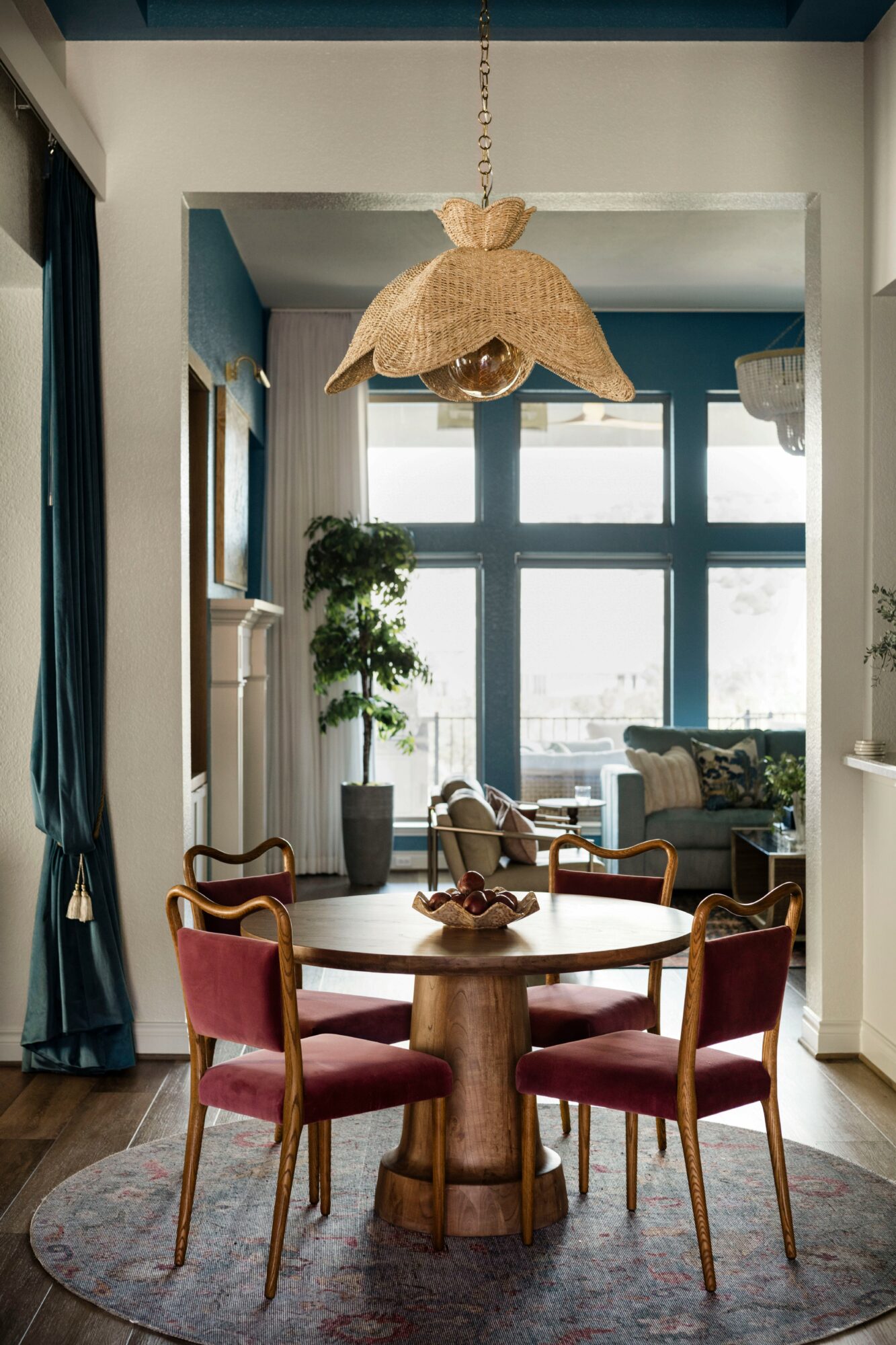 Dining area with round wooden table, four red chairs, large window, potted plant, and hanging light fixture.