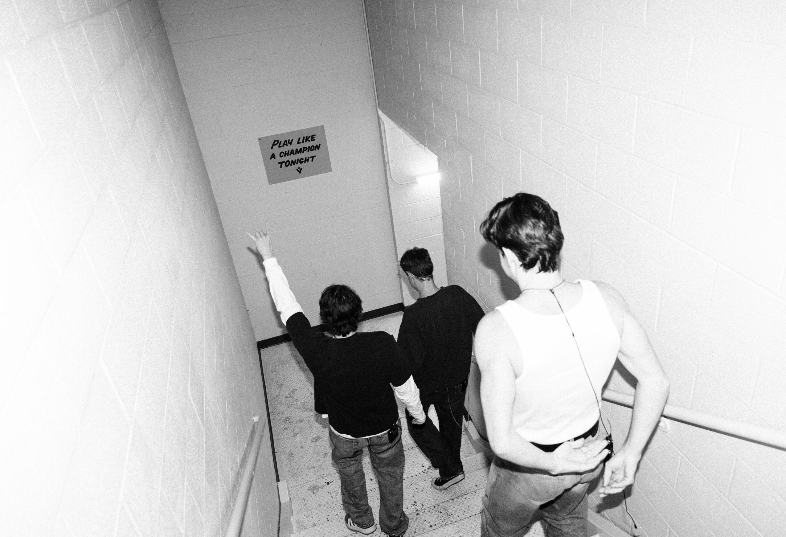 Three people walking down a stairwell with a sign on the wall, black and white photo.