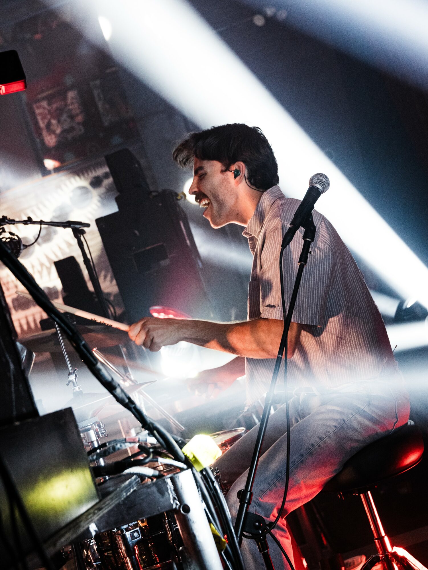 A young man playing keyboard and singing into a microphone during a live music performance, with stage lights and equipment around him.