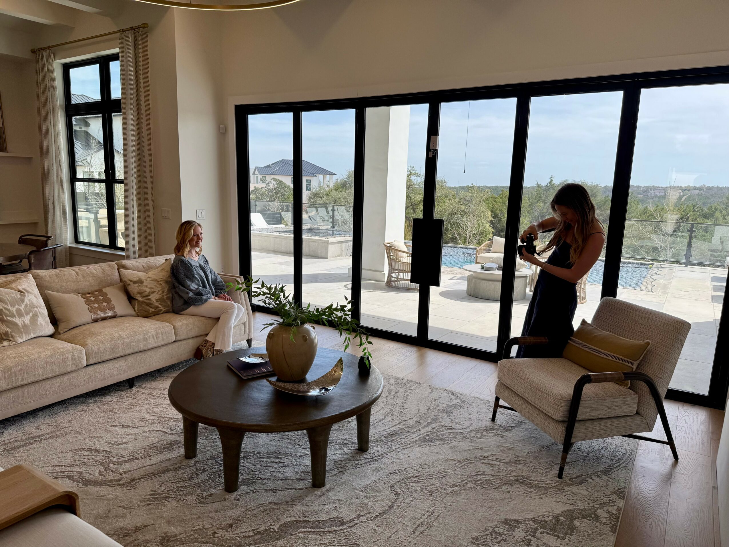Living room with large sliding glass doors, a woman sitting on a sofa, and a person playing violin, with outdoor view.