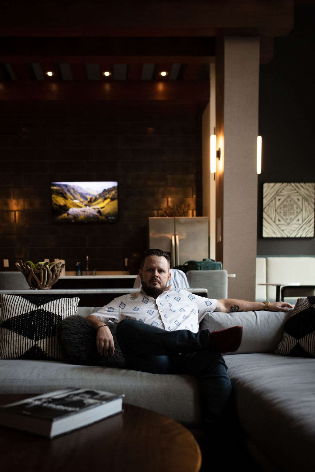 Man sitting on a sofa in a modern living room with a television and decorative elements behind him.