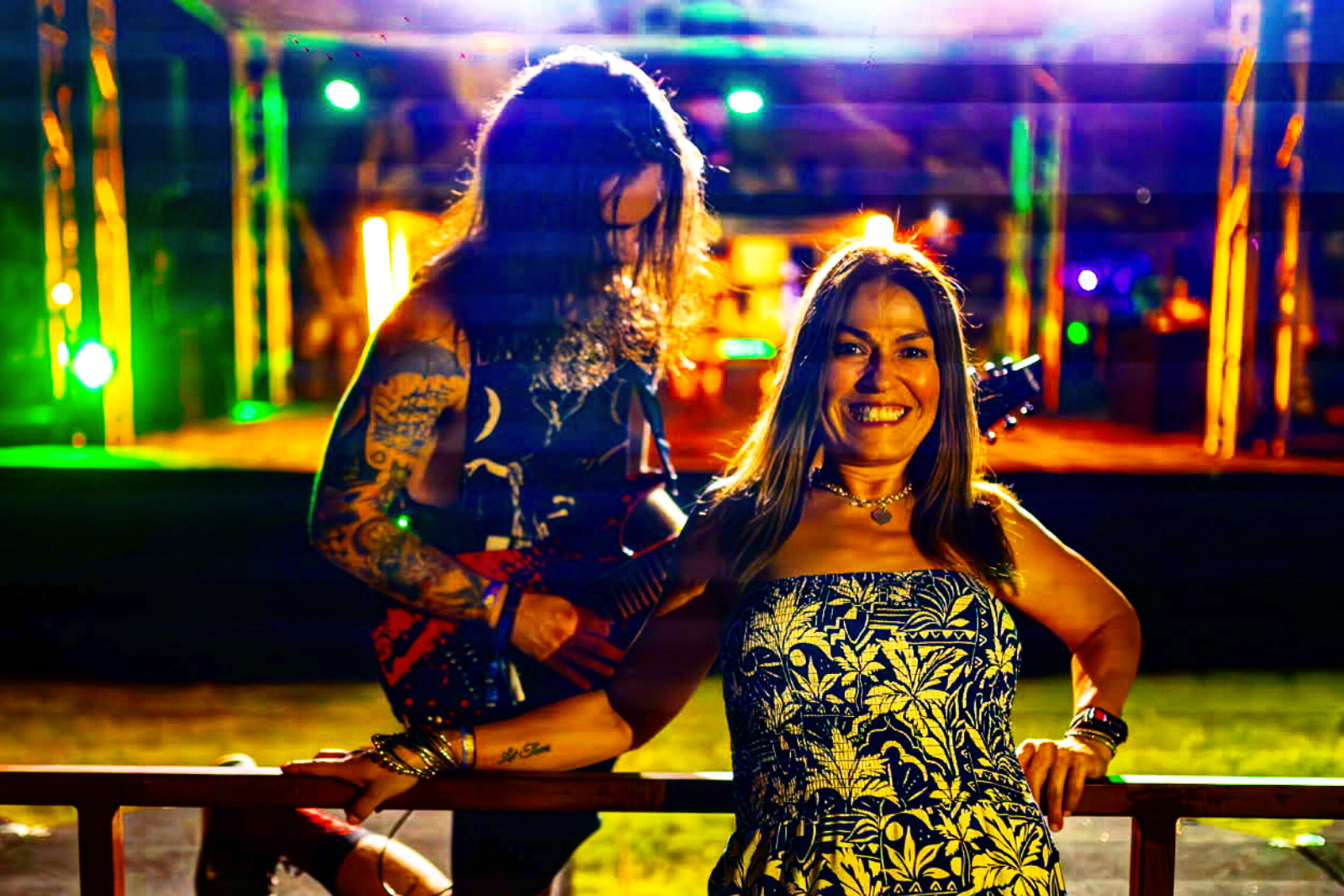 Two women smiling and posing outdoors at night with colorful lights in the background.