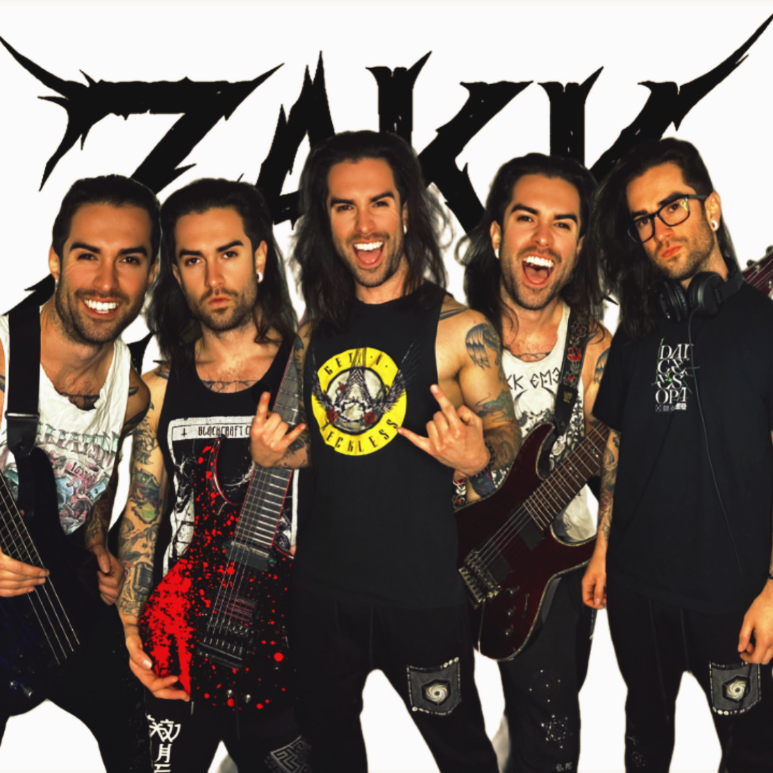 Group of five men posing with guitars in front of a logo, smiling and making gestures, with a white background.