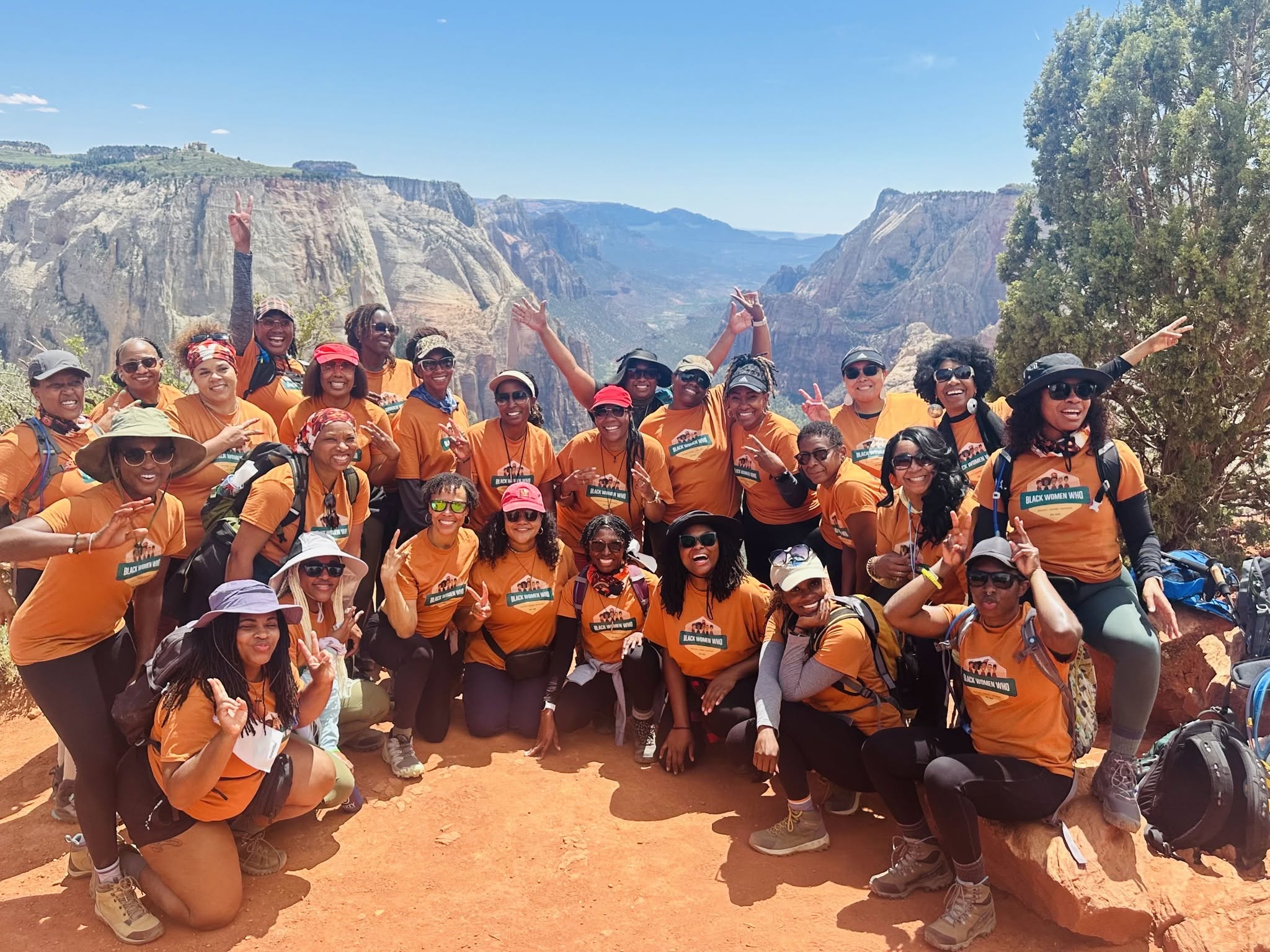 Group of people wearing orange shirts and hats, posing outdoors with canyon cliffs in the background.