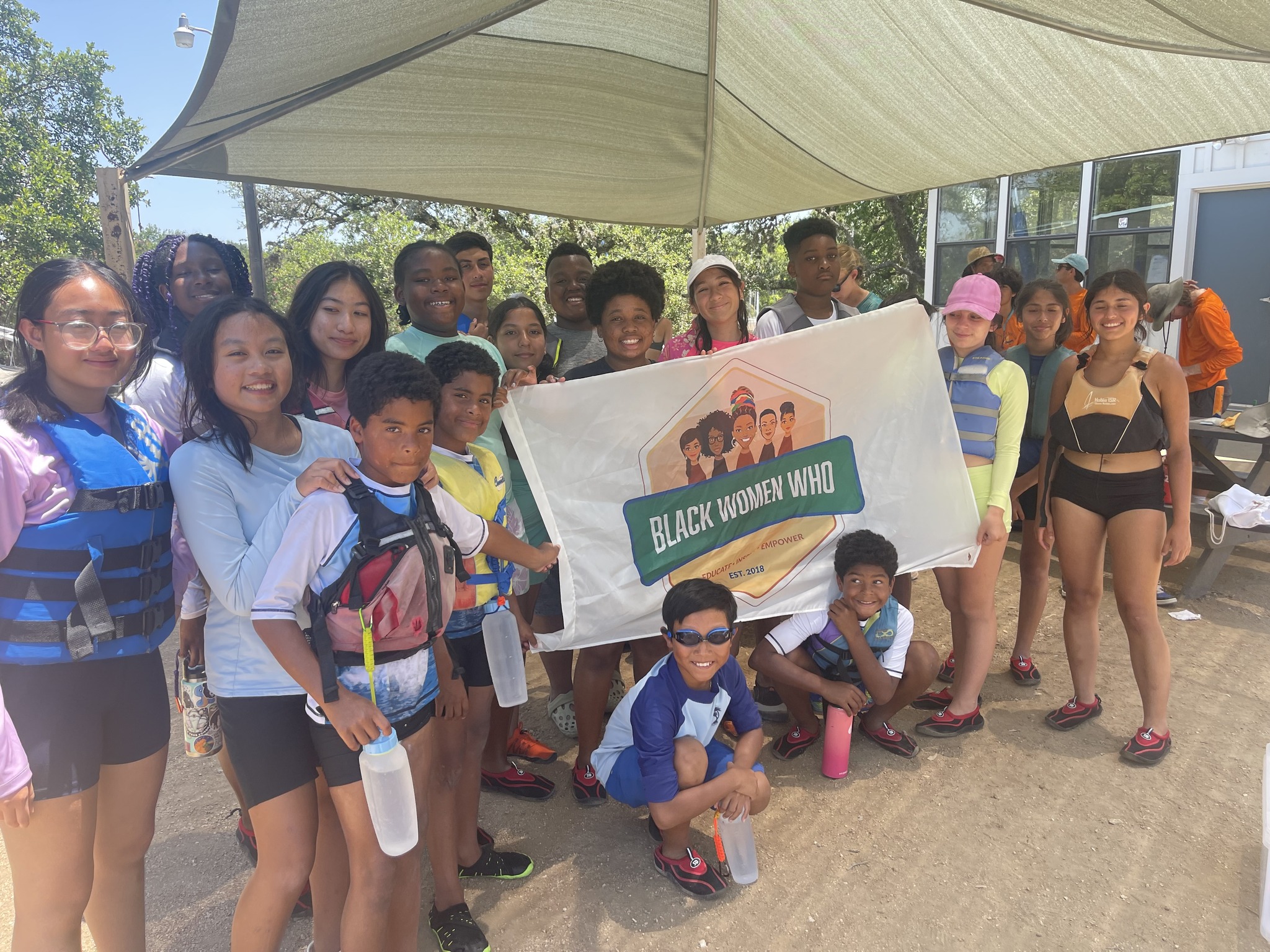 Group of diverse women and children outdoors holding a banner that reads 'Black Women Who'.