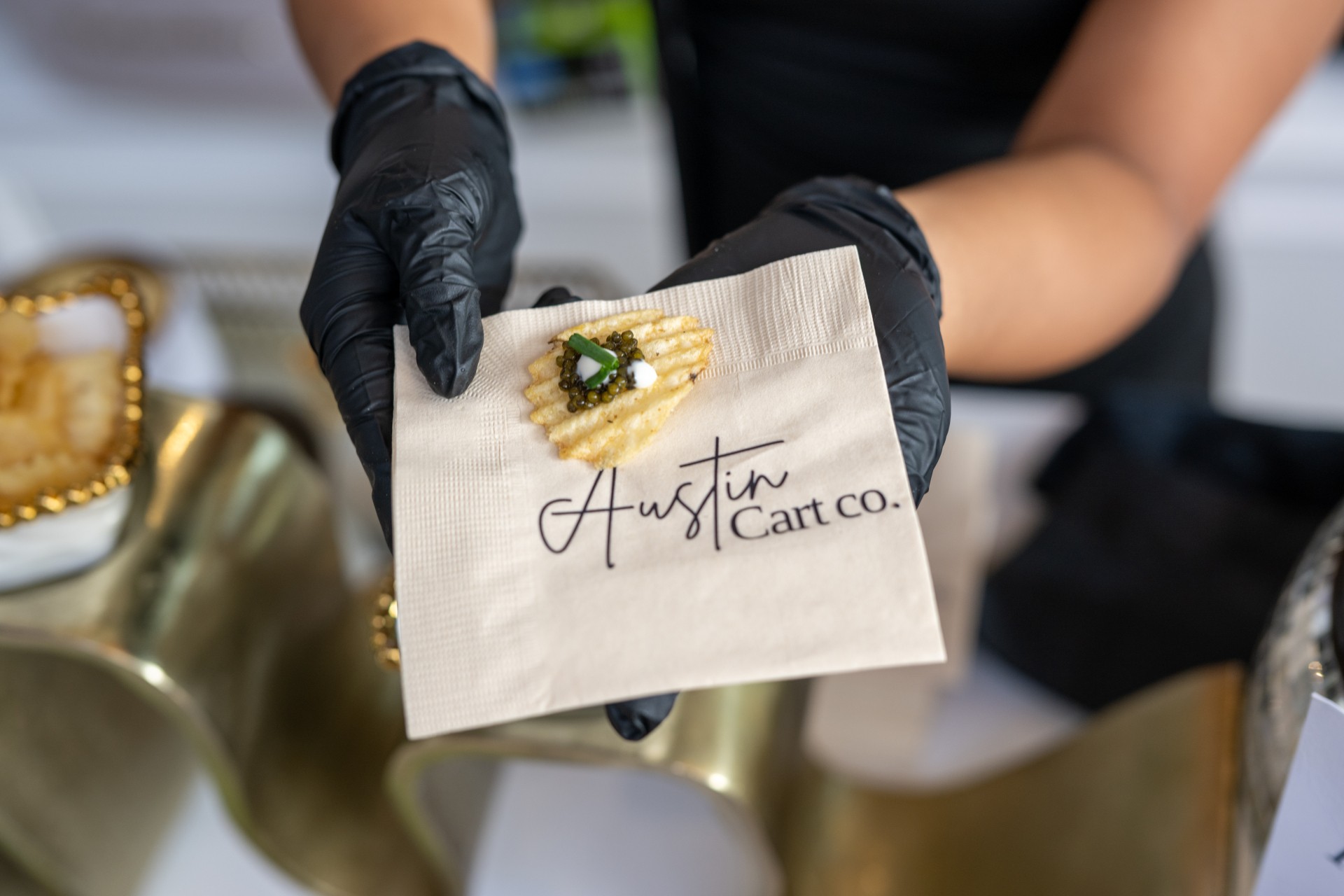 Person wearing black gloves holding a small beige bag with a gold brooch and handwritten note reading 'Austin Cart Co.'