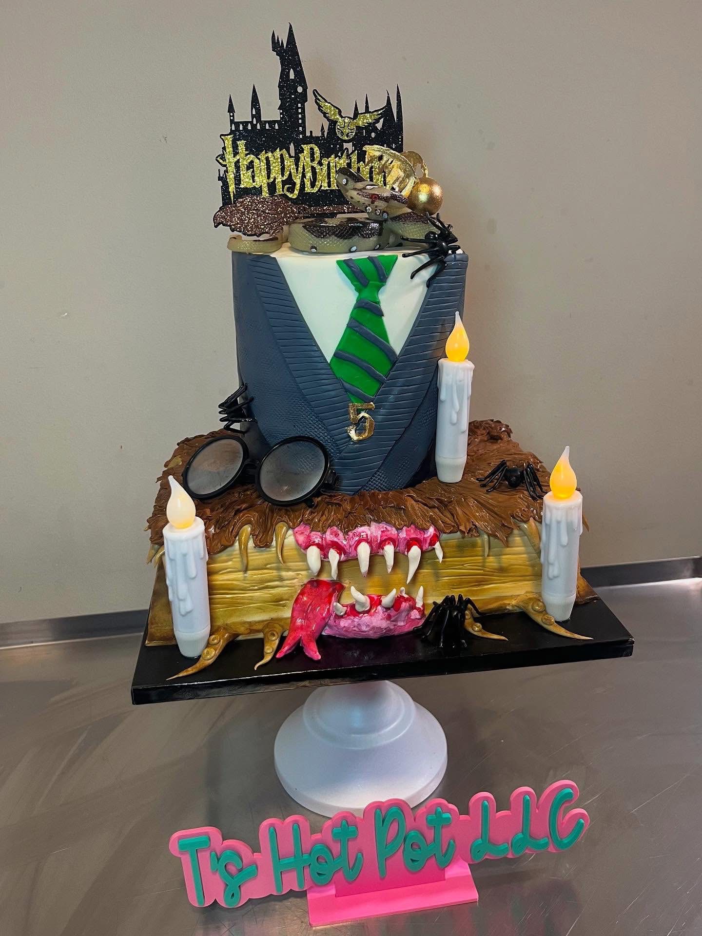 Cake with Harry Potter theme, featuring a Hogwarts castle topper, glasses, wand, and candles, on a black base with pink lettering.