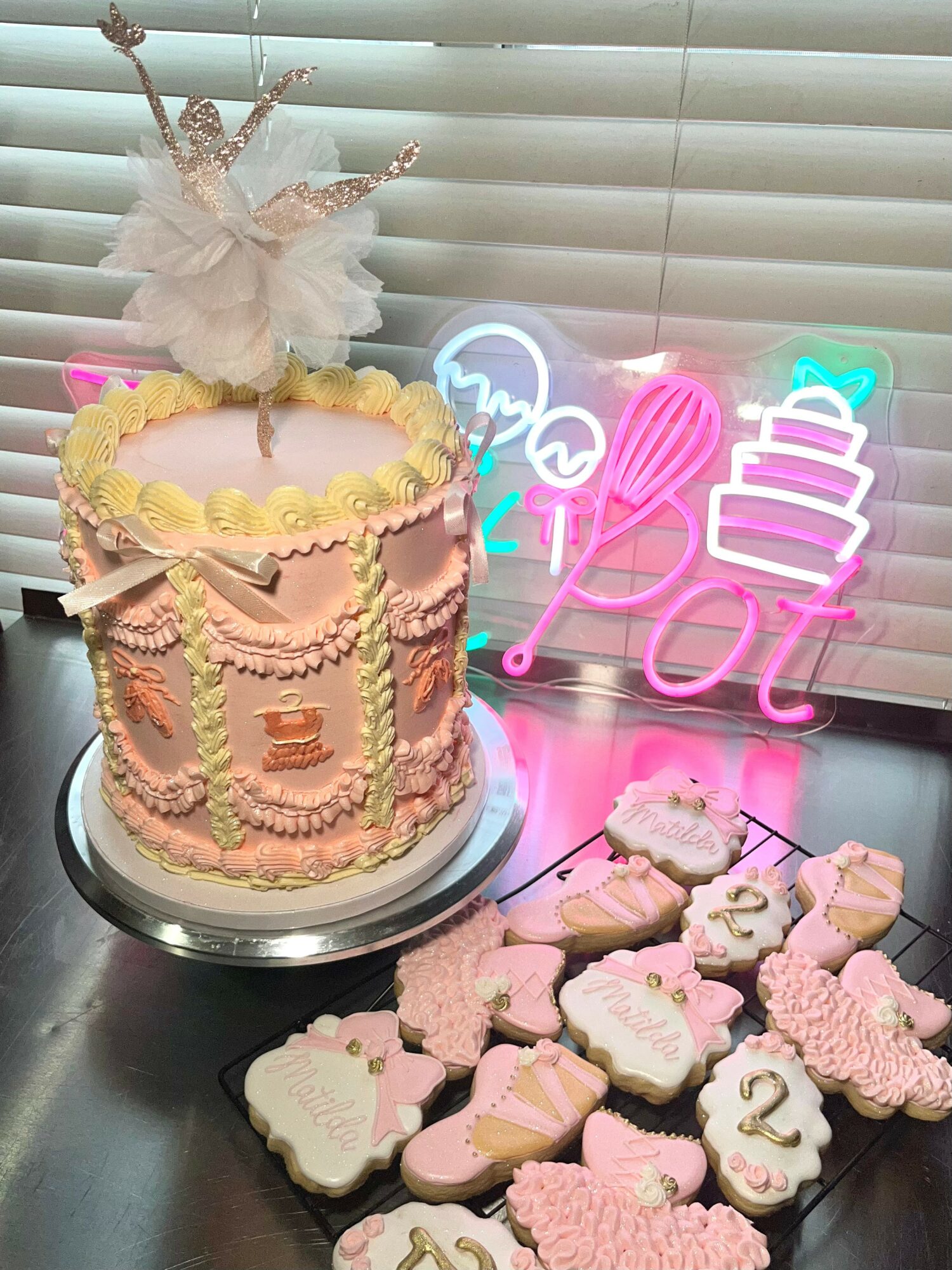 Decorative cake with a unicorn topper, surrounded by pink and white cookies, and neon signs in the background.