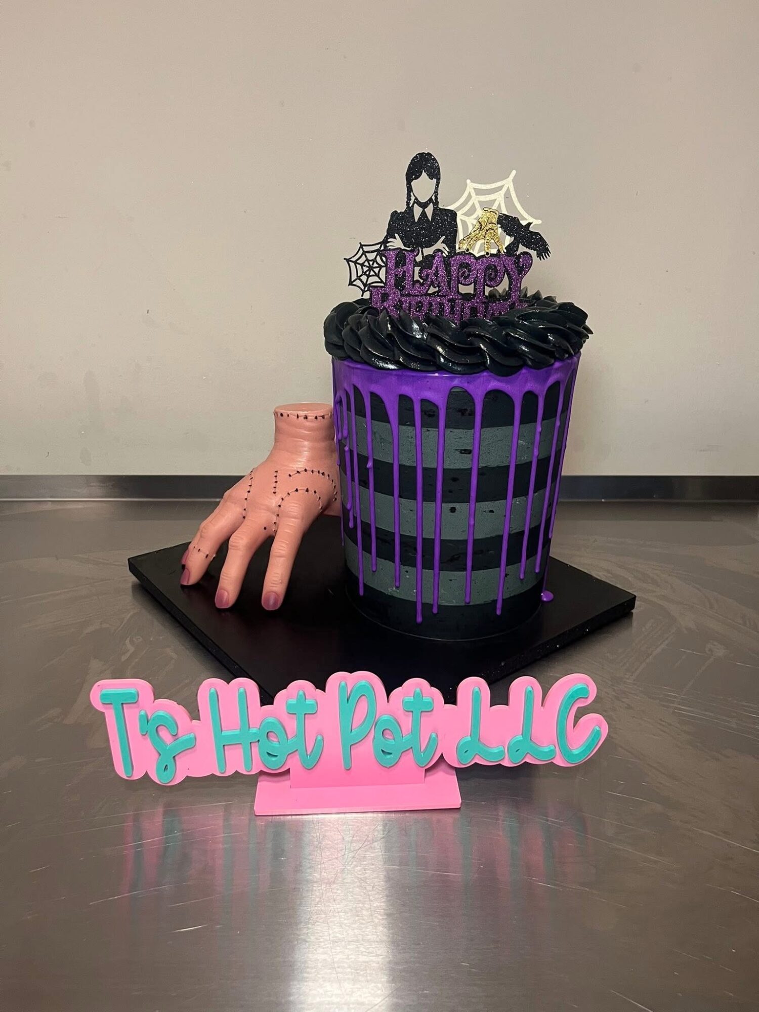 A Halloween-themed cake with purple and black decorations, a pink hand, and a sign reading 