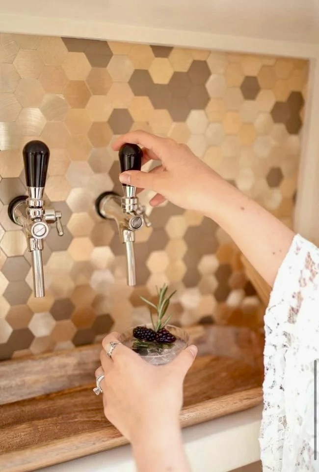 Person filling a small plant pot with liquid from a tap, with a honeycomb-patterned wall in the background.