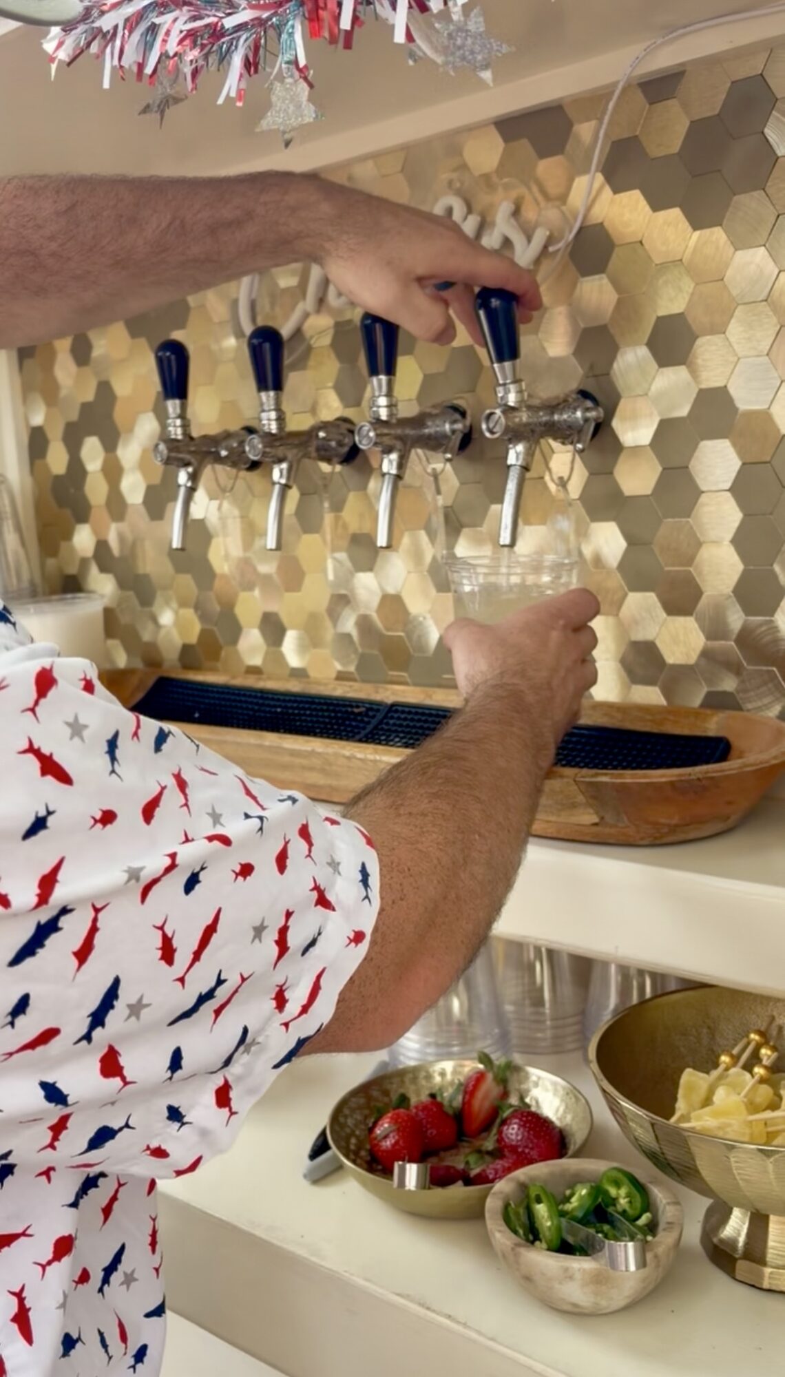Person filling a glass from a row of beer taps in a bar or pub, with a honeycomb-patterned wall in the background.