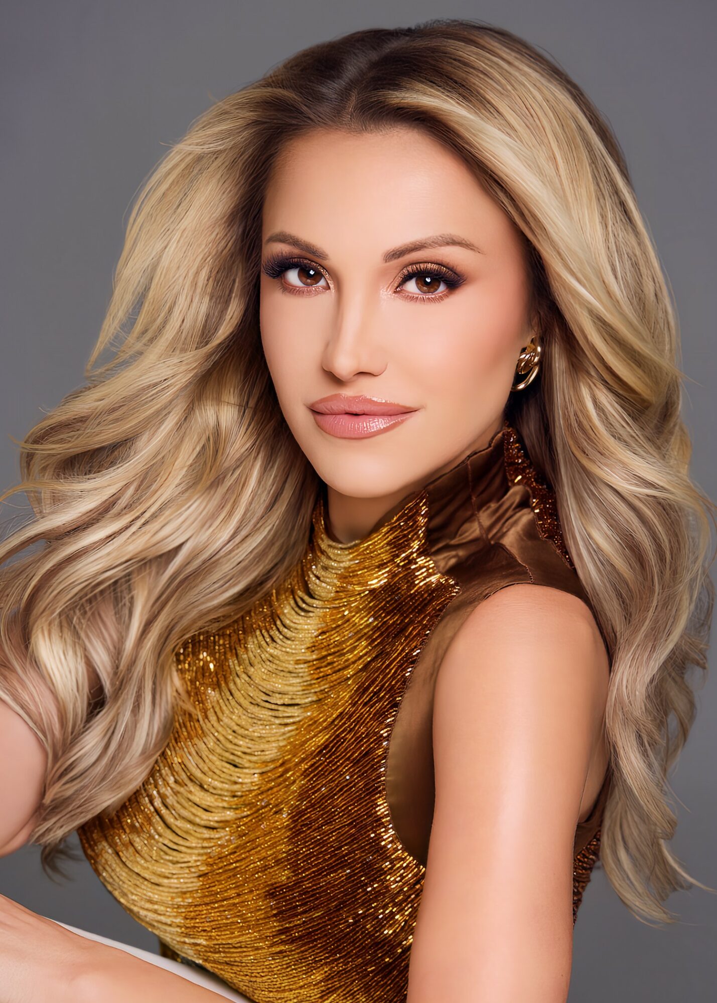 Portrait of a woman with long, wavy blonde hair wearing a gold and brown dress, looking at the camera.