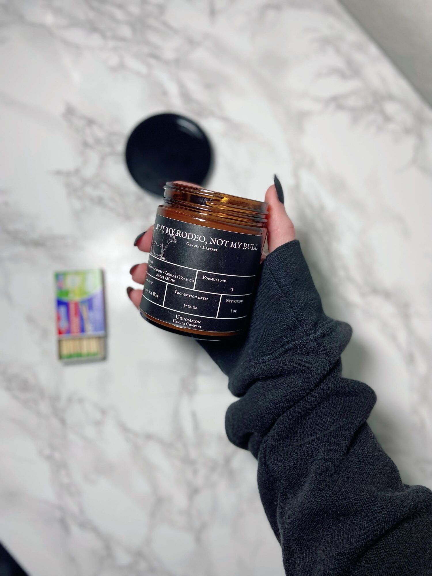 Person holding an open jar of supplement or medication on a marble surface, with a black lid nearby and a colorful box in the background.