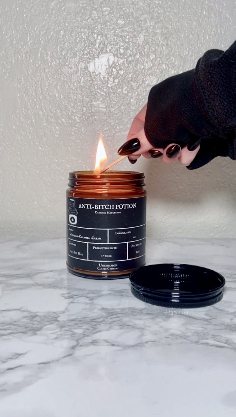 Person lighting a candle with a match, black nail polish, on a marble surface, against a textured wall.